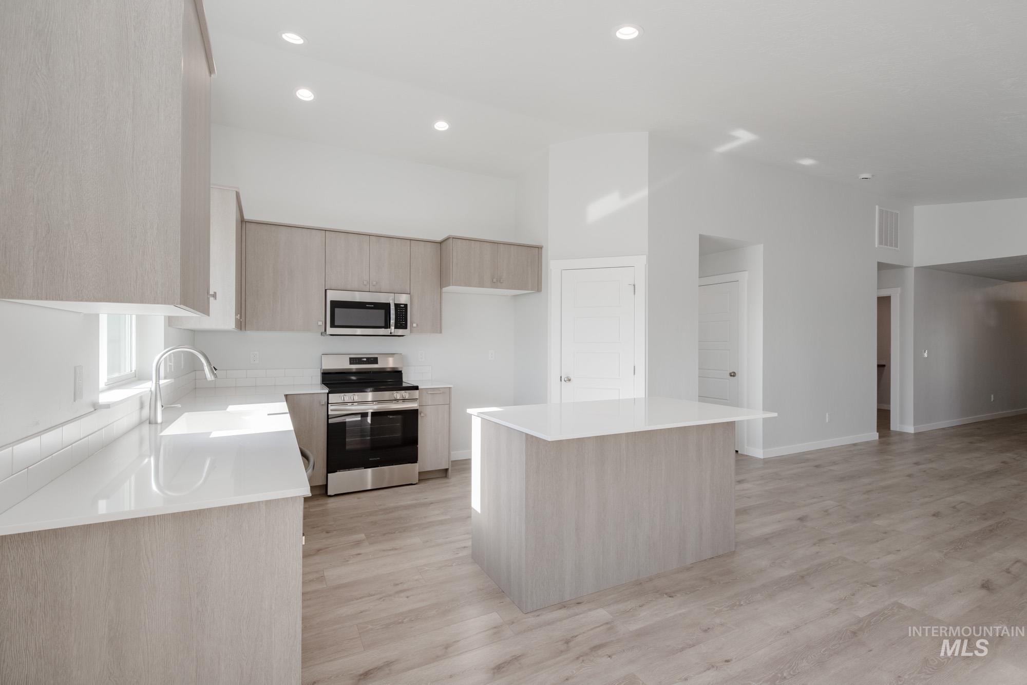 Kitchen featuring light brown cabinets, stainless steel appliances, a kitchen island, light wood finished floors, and recessed lighting