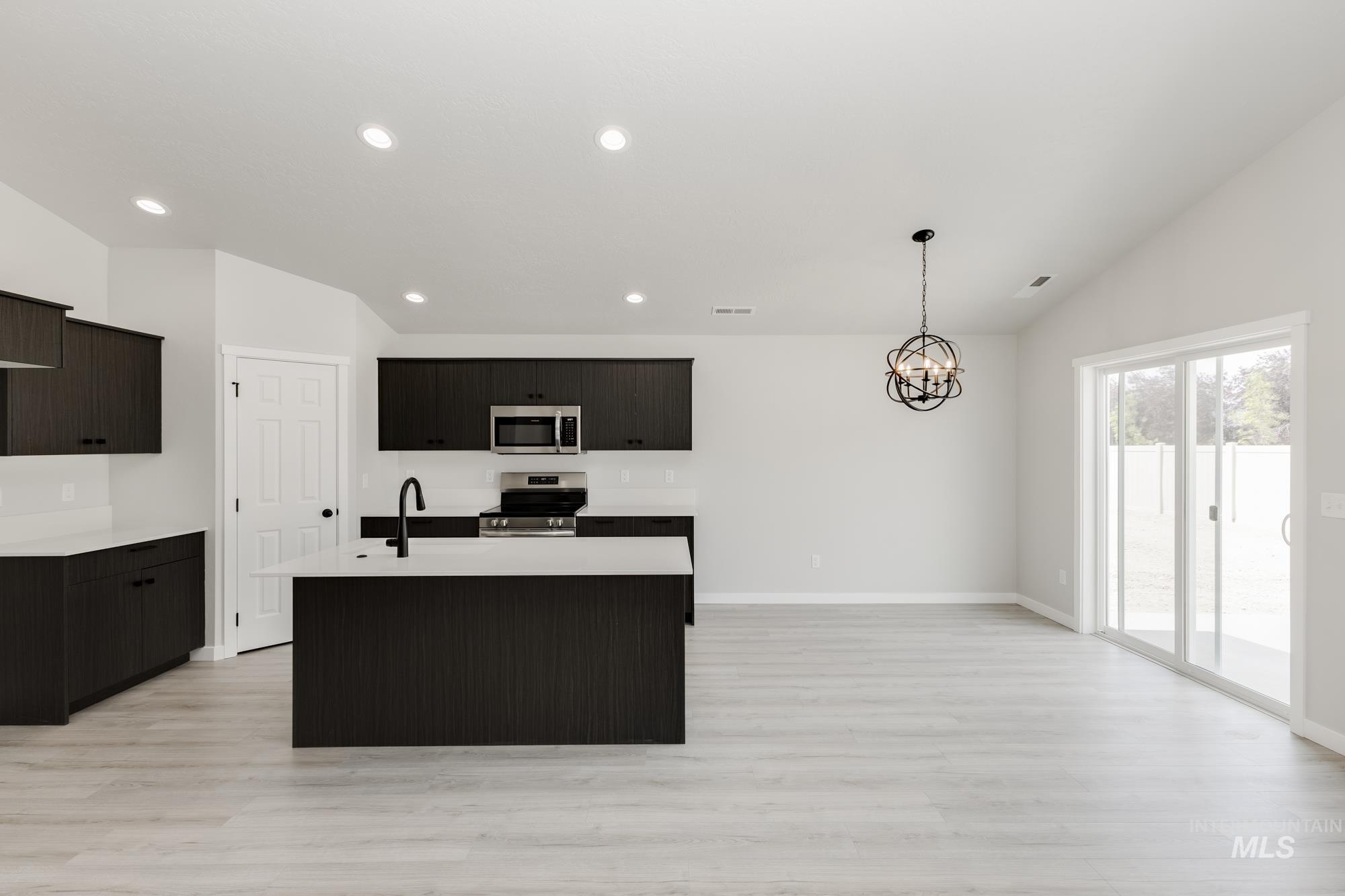 Kitchen featuring an island with sink, vaulted ceiling, appliances with stainless steel finishes, hanging light fixtures, and a chandelier