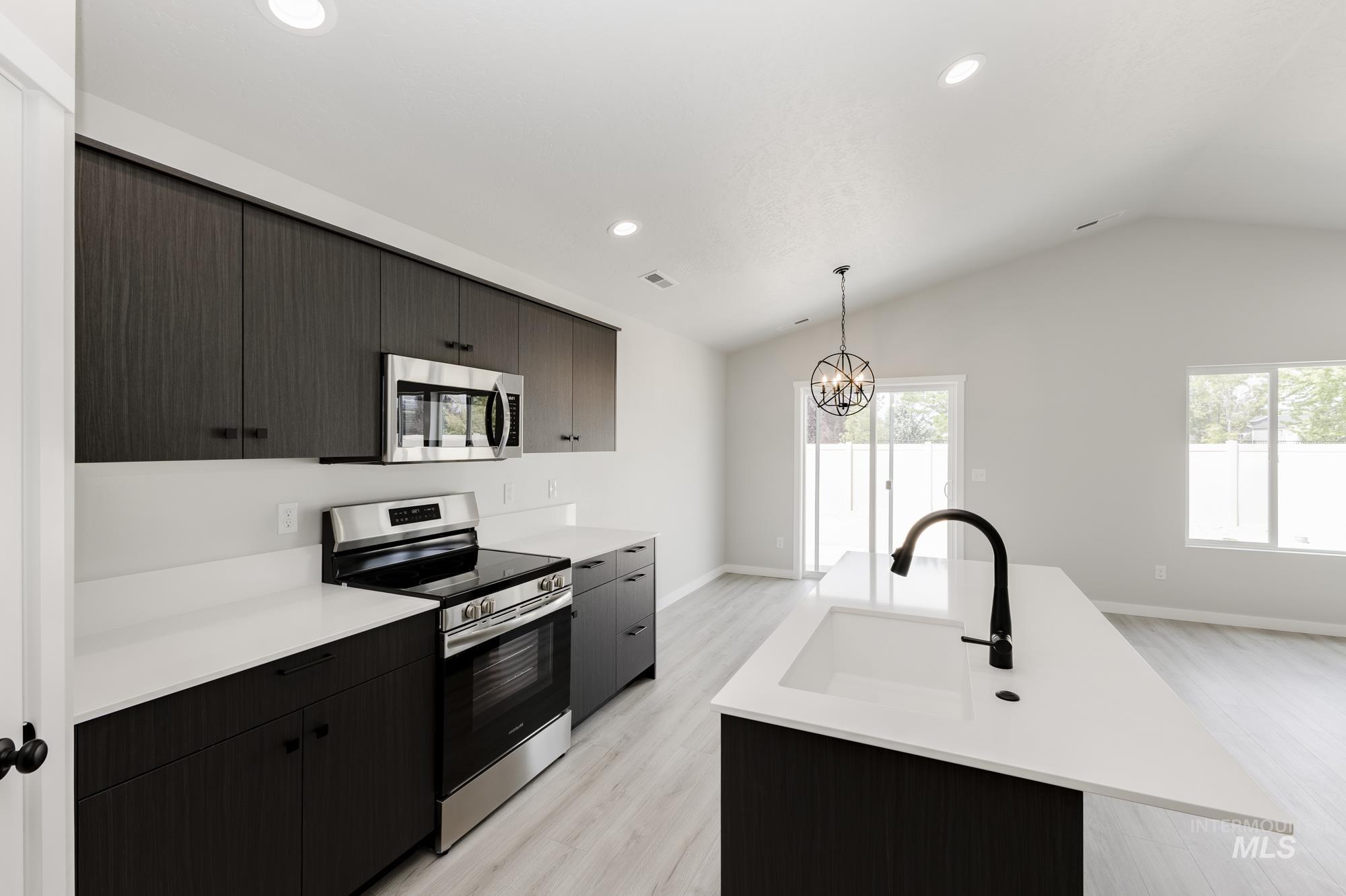 Kitchen with appliances with stainless steel finishes, modern cabinets, hanging light fixtures, an island with sink, and vaulted ceiling