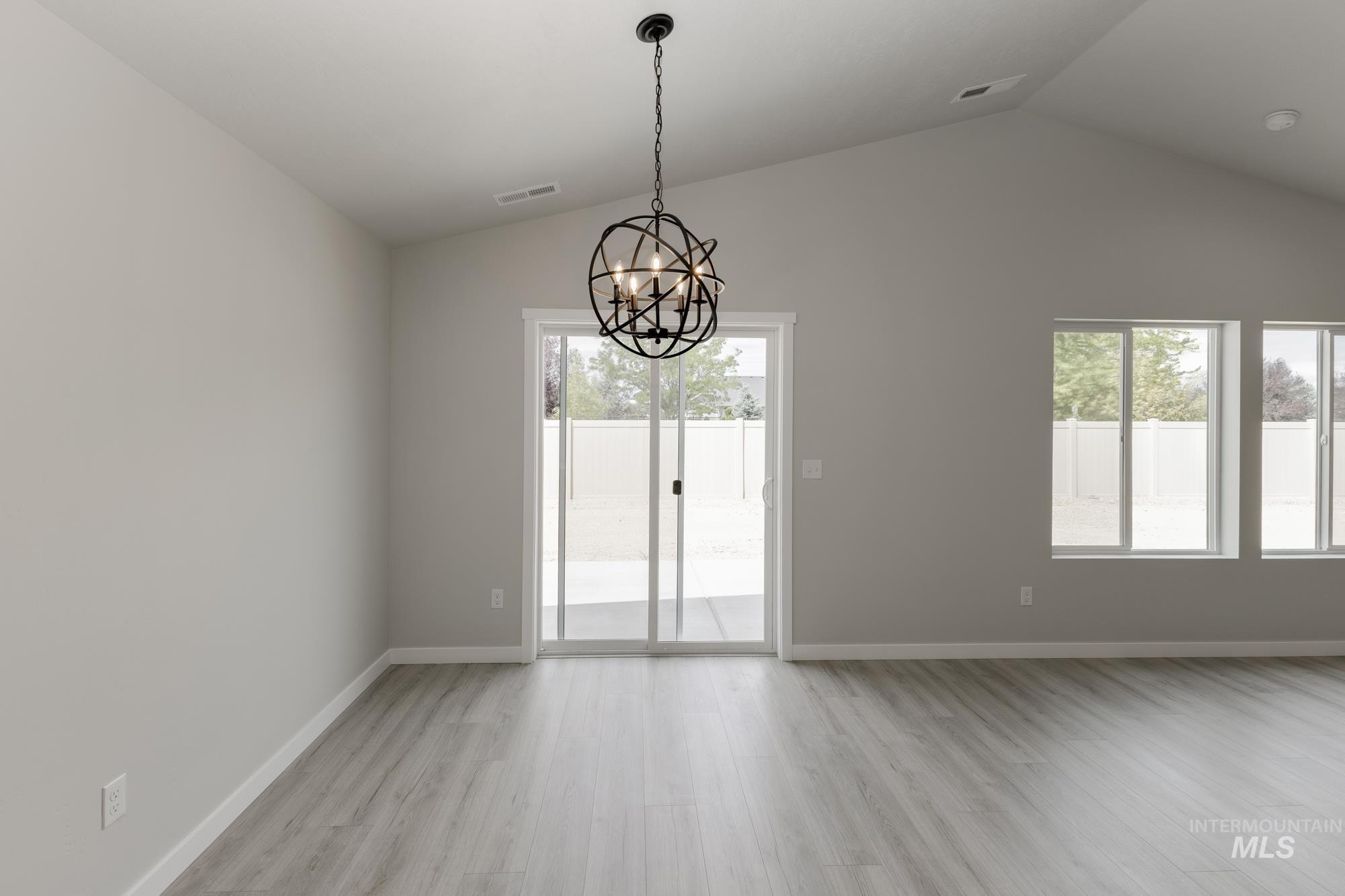 Unfurnished room featuring lofted ceiling, light wood-style floors, a chandelier, and plenty of natural light