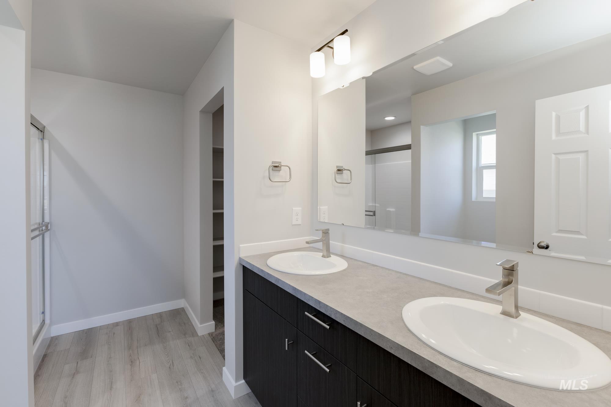 Full bathroom featuring a shower stall, double vanity, light wood-type flooring, and a spacious closet