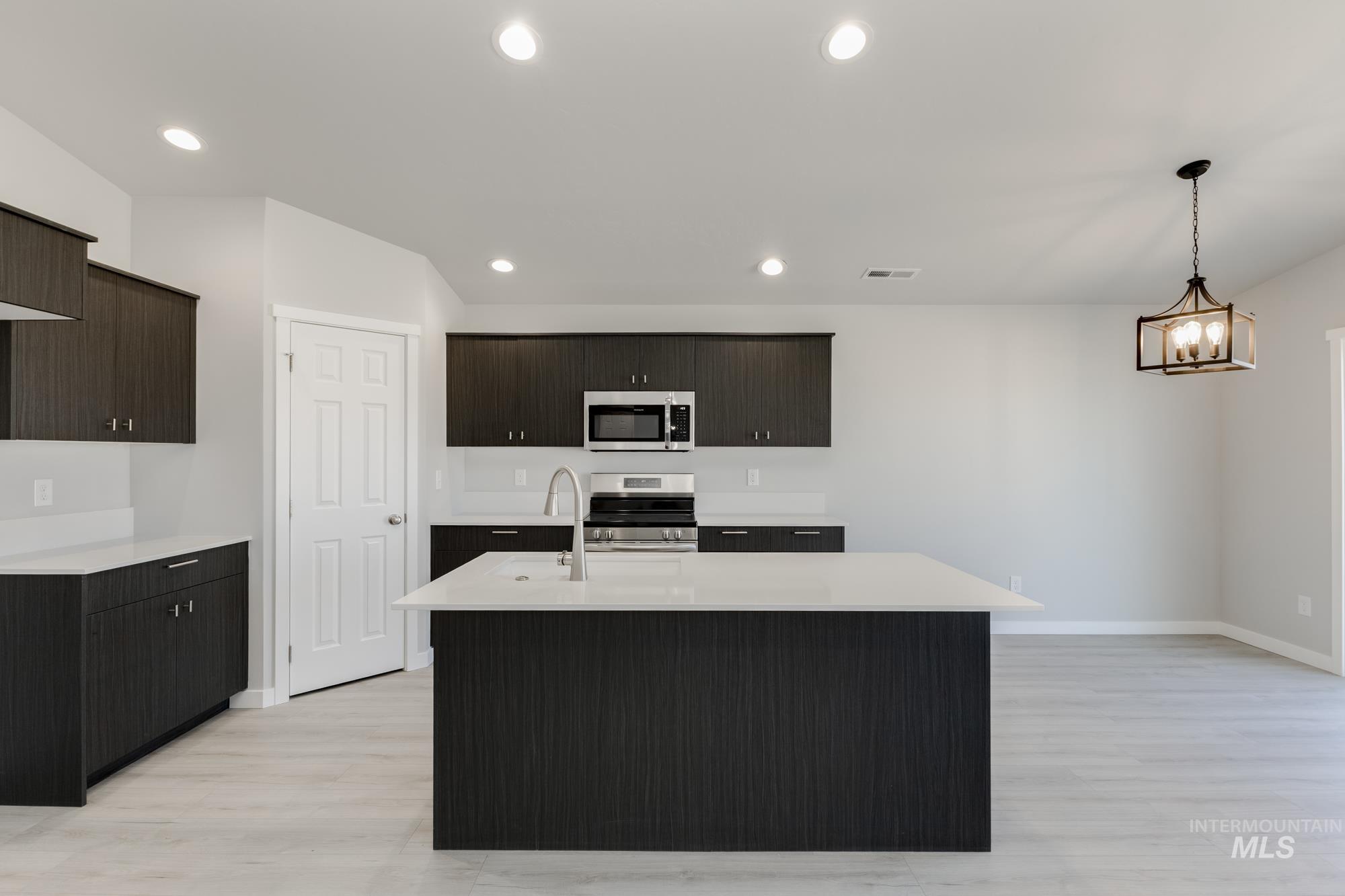 Kitchen with decorative light fixtures, appliances with stainless steel finishes, an island with sink, light wood finished floors, and recessed lighting