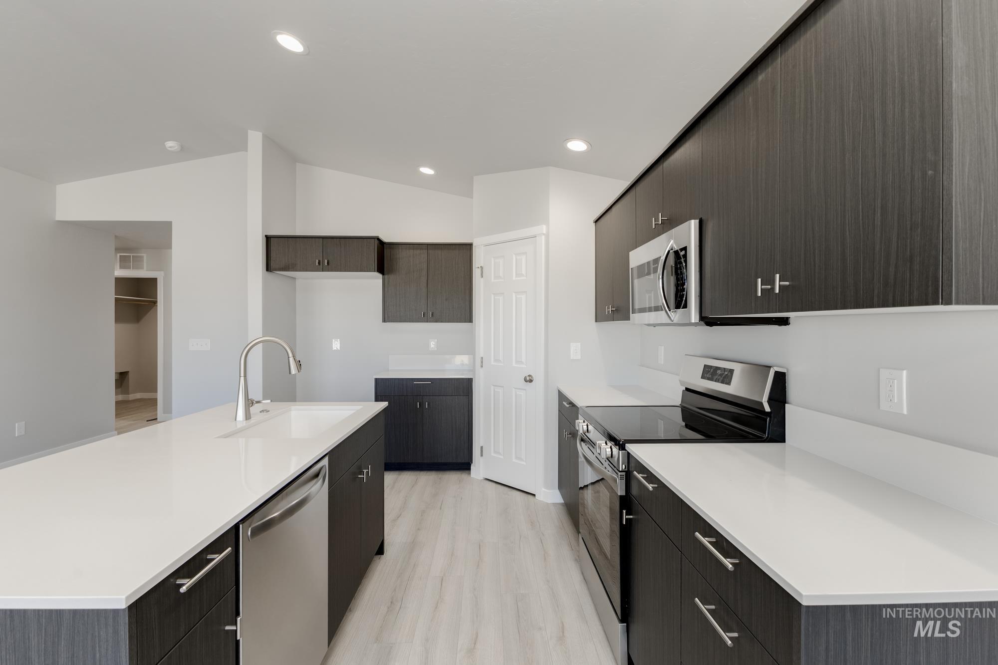 Kitchen featuring appliances with stainless steel finishes, light wood finished floors, a kitchen island with sink, lofted ceiling, and recessed lighting