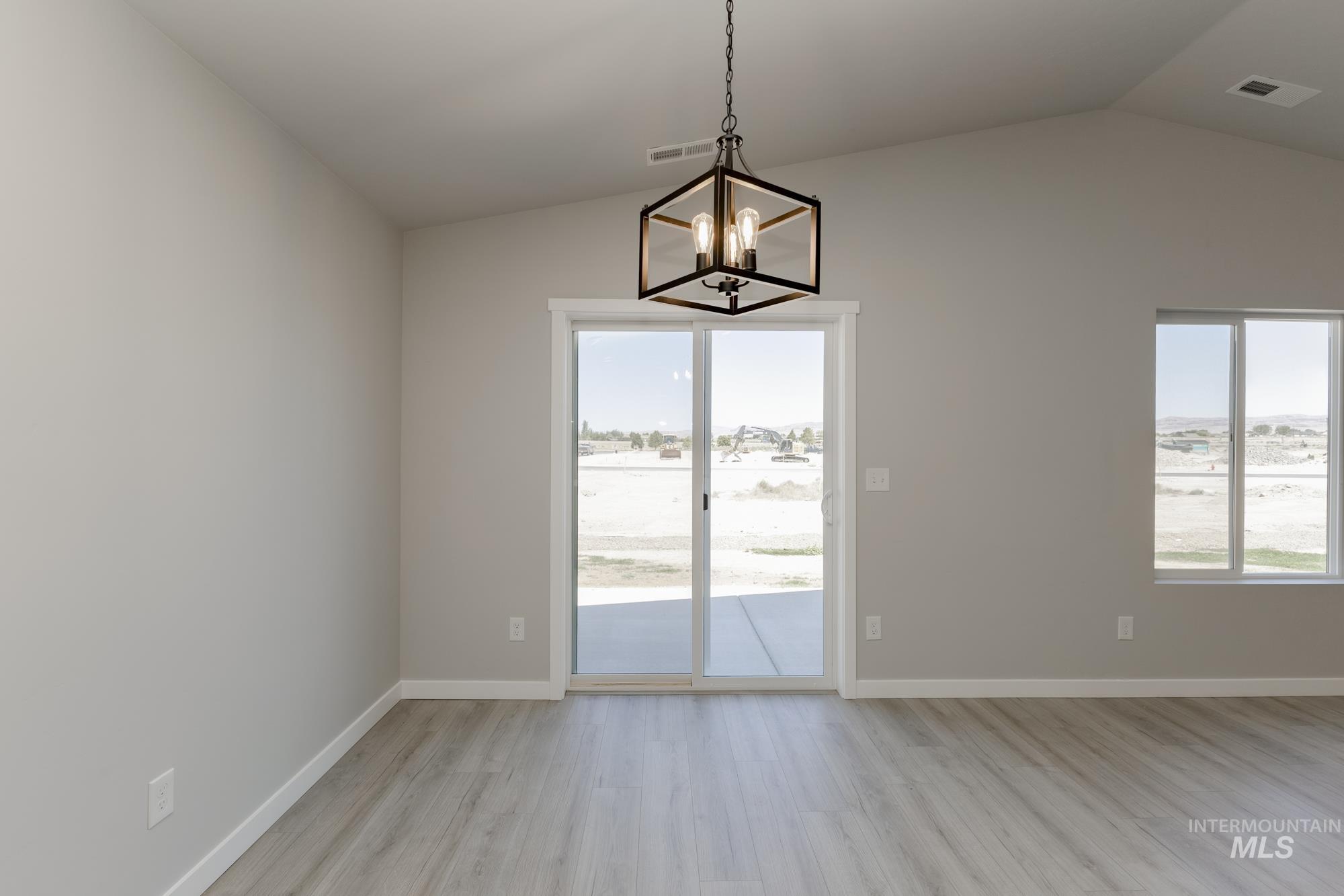 Unfurnished dining area featuring light wood-type flooring, healthy amount of natural light, vaulted ceiling, and a chandelier