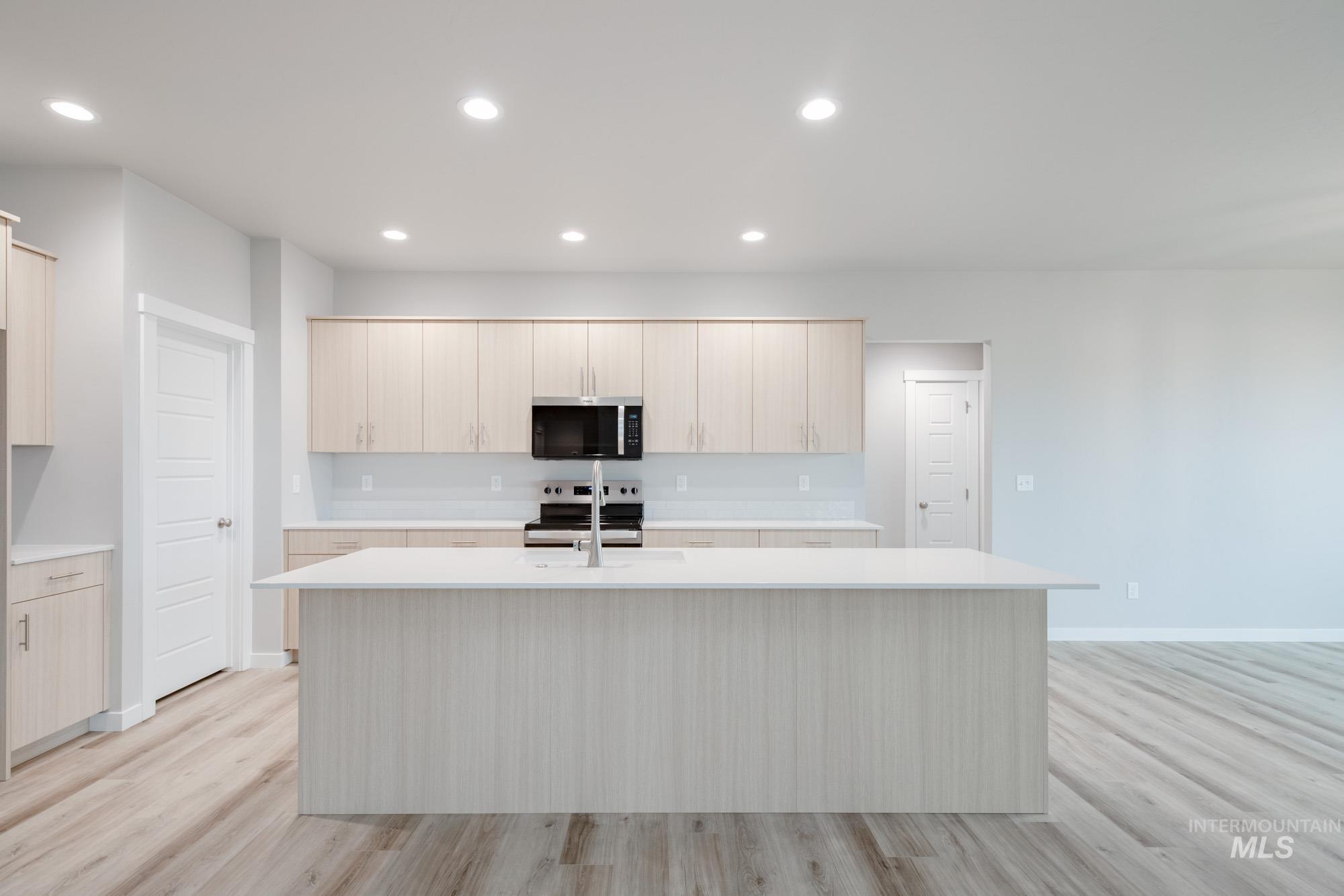 Kitchen with light brown cabinets, appliances with stainless steel finishes, light wood finished floors, and recessed lighting