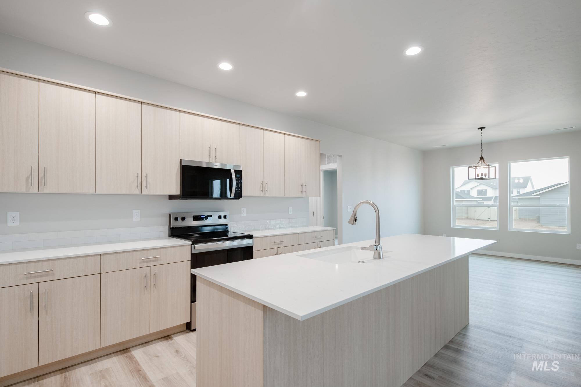 Kitchen with light brown cabinets, appliances with stainless steel finishes, hanging light fixtures, recessed lighting, and light wood-type flooring