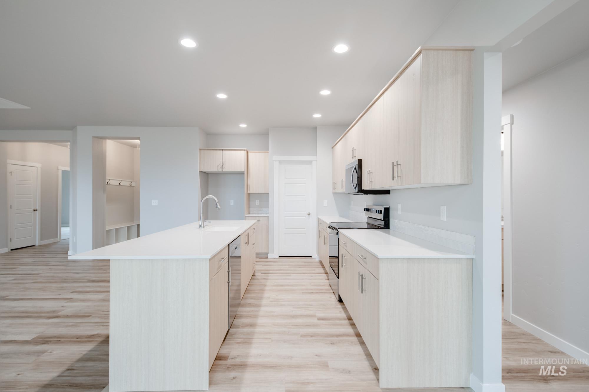 Kitchen with appliances with stainless steel finishes, a center island with sink, recessed lighting, light wood-style flooring, and light stone counters