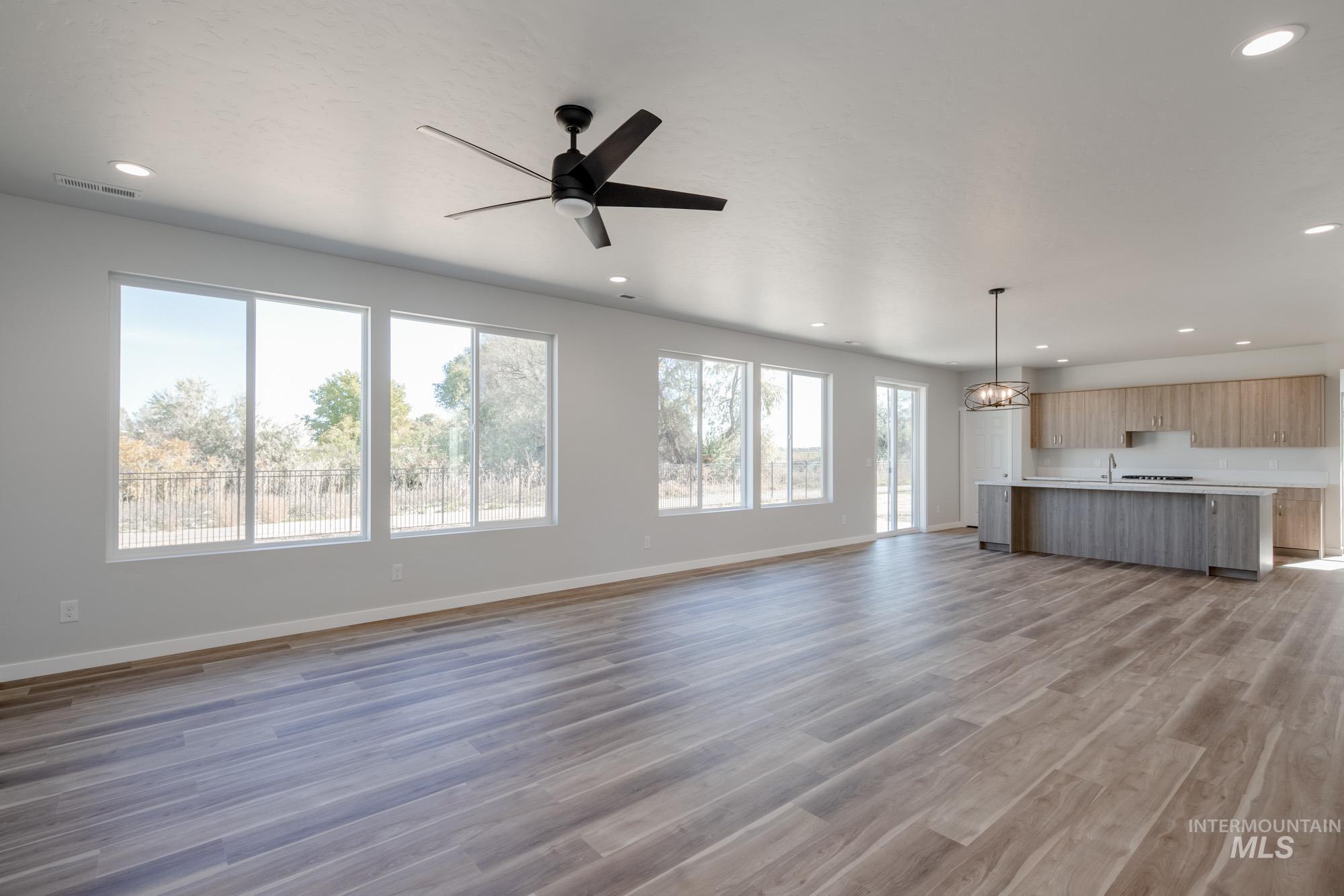 Unfurnished living room featuring dark wood finished floors, recessed lighting, ceiling fan, and a chandelier