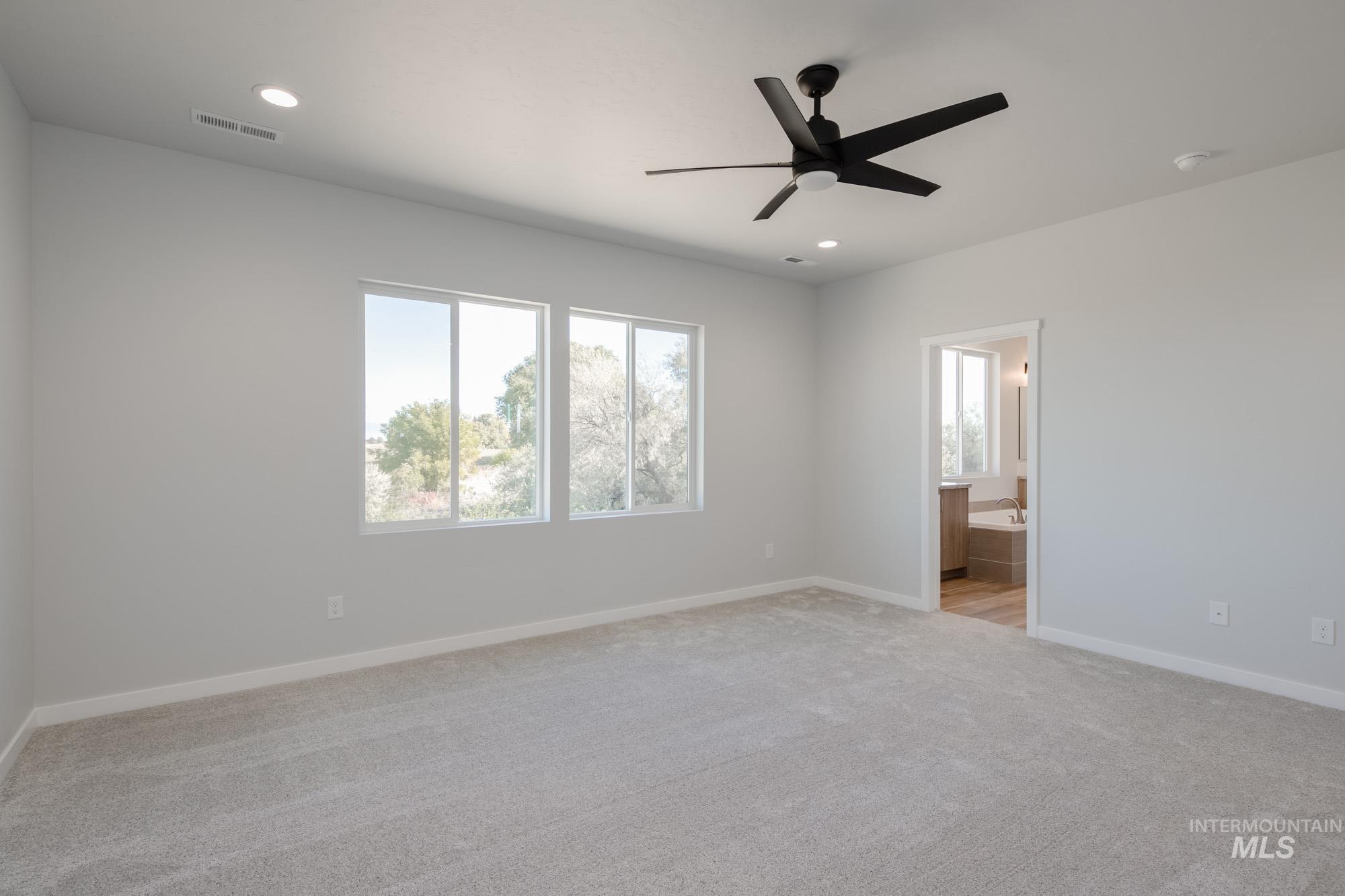 Unfurnished bedroom featuring multiple windows, light carpet, a ceiling fan, recessed lighting, and ensuite bath