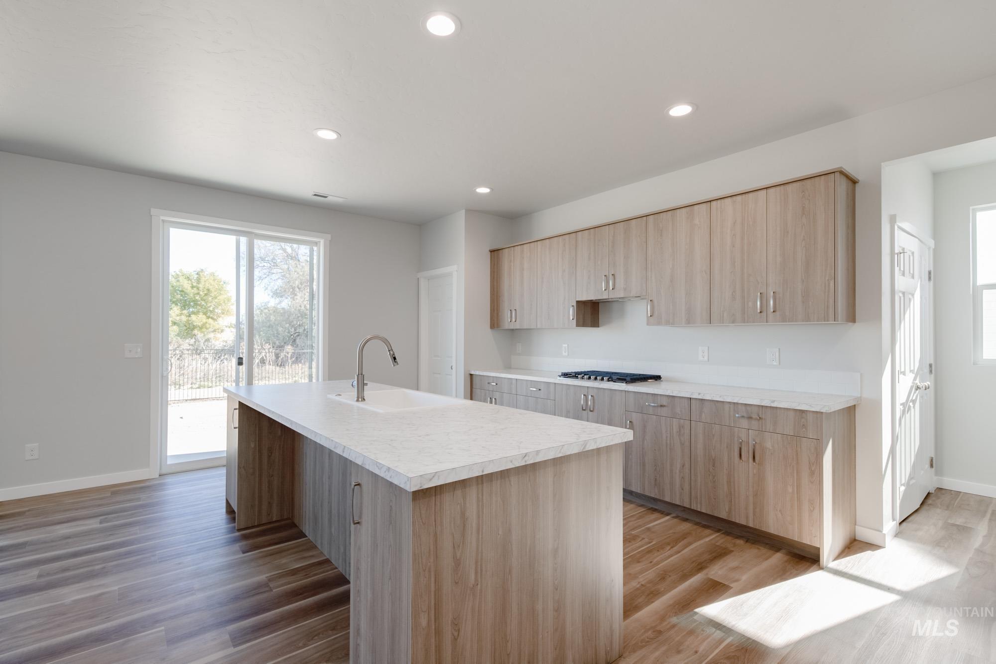 Kitchen with light brown cabinets, light countertops, light wood finished floors, an island with sink, and recessed lighting