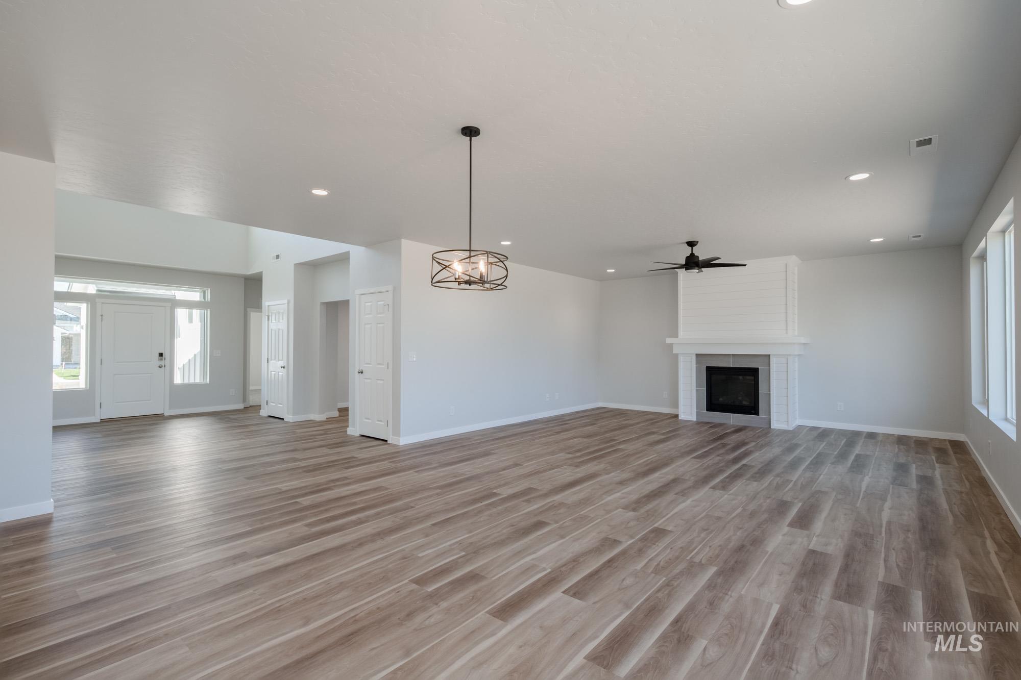 Unfurnished living room featuring a tile fireplace, light wood finished floors, a chandelier, recessed lighting, and a ceiling fan