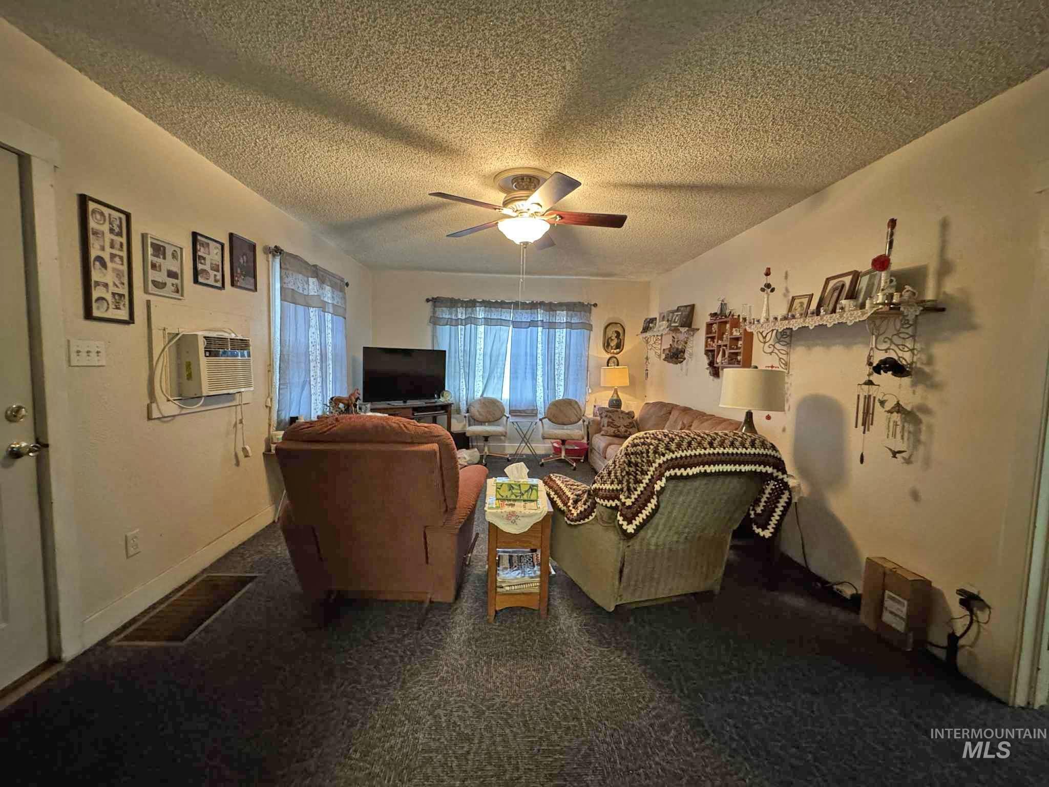 Living area featuring a textured ceiling, ceiling fan, and an AC wall unit
