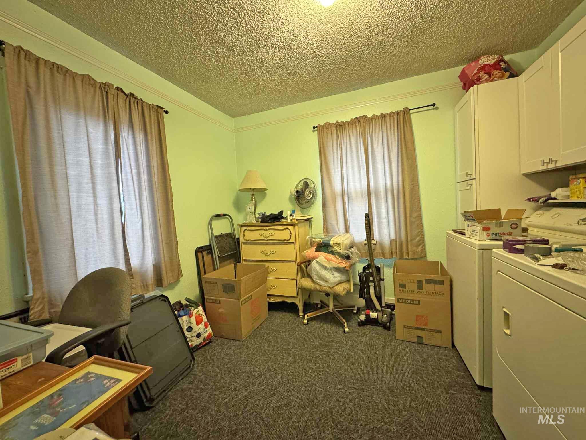 Office space featuring a textured ceiling, dark colored carpet, healthy amount of natural light, and separate washer and dryer