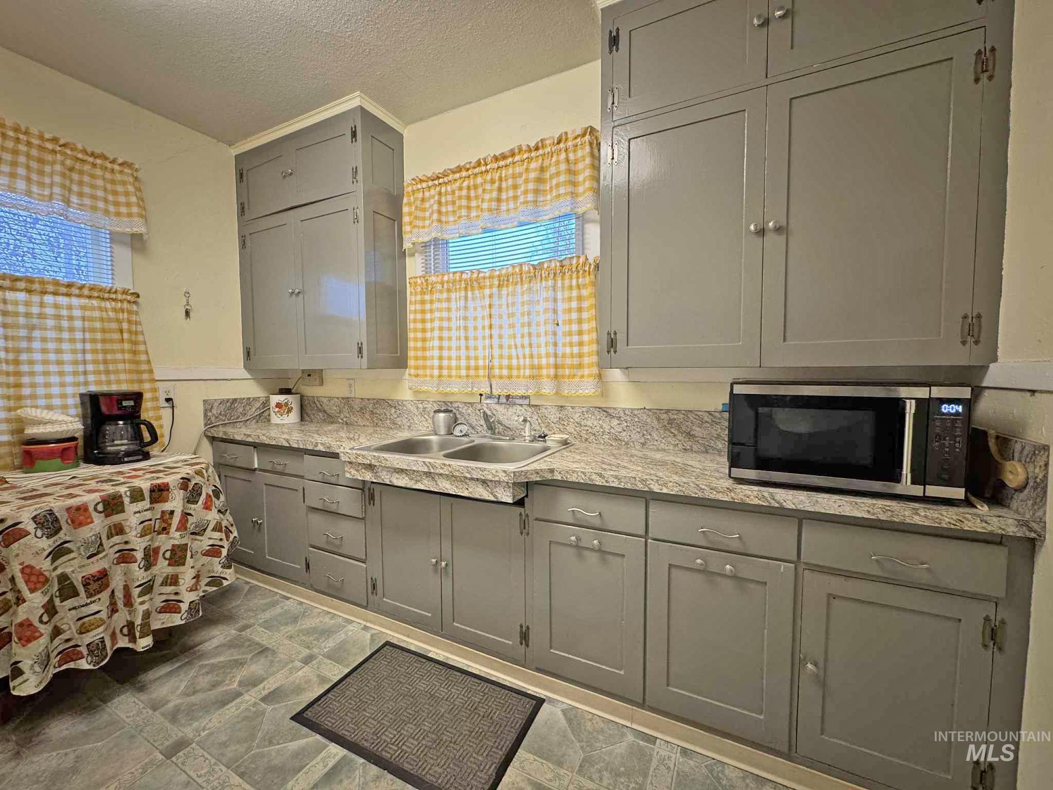 Kitchen featuring gray cabinets, a textured ceiling, stainless steel microwave, and stone finish flooring