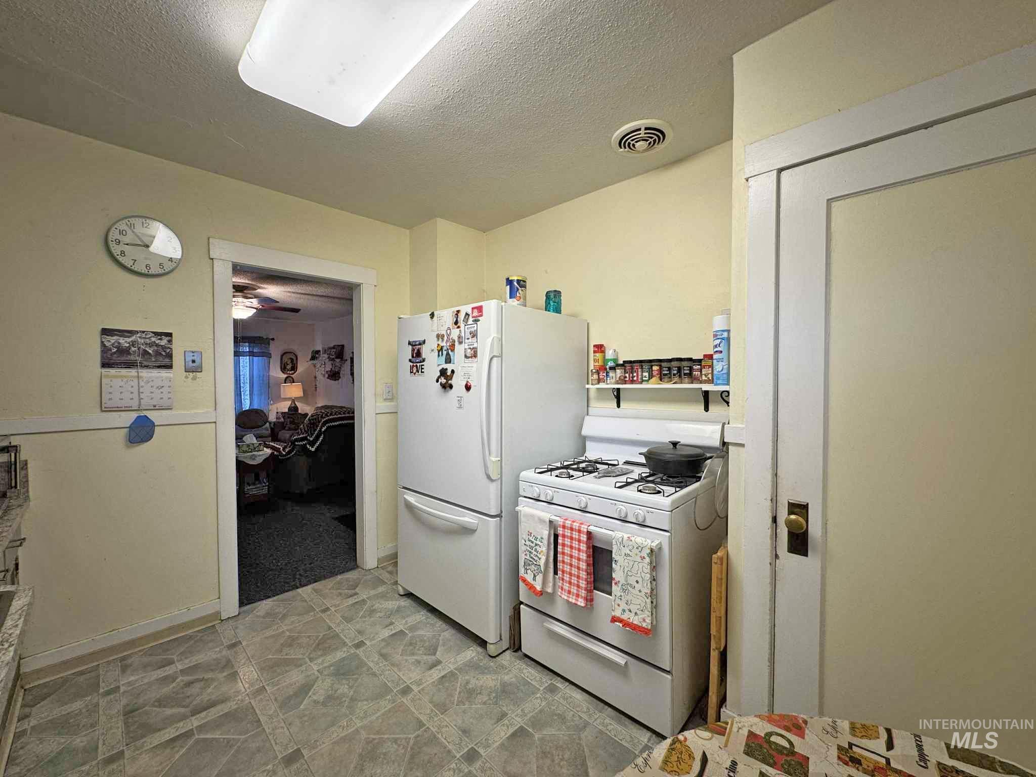 Kitchen featuring white appliances, a textured ceiling, light floors, and ceiling fan