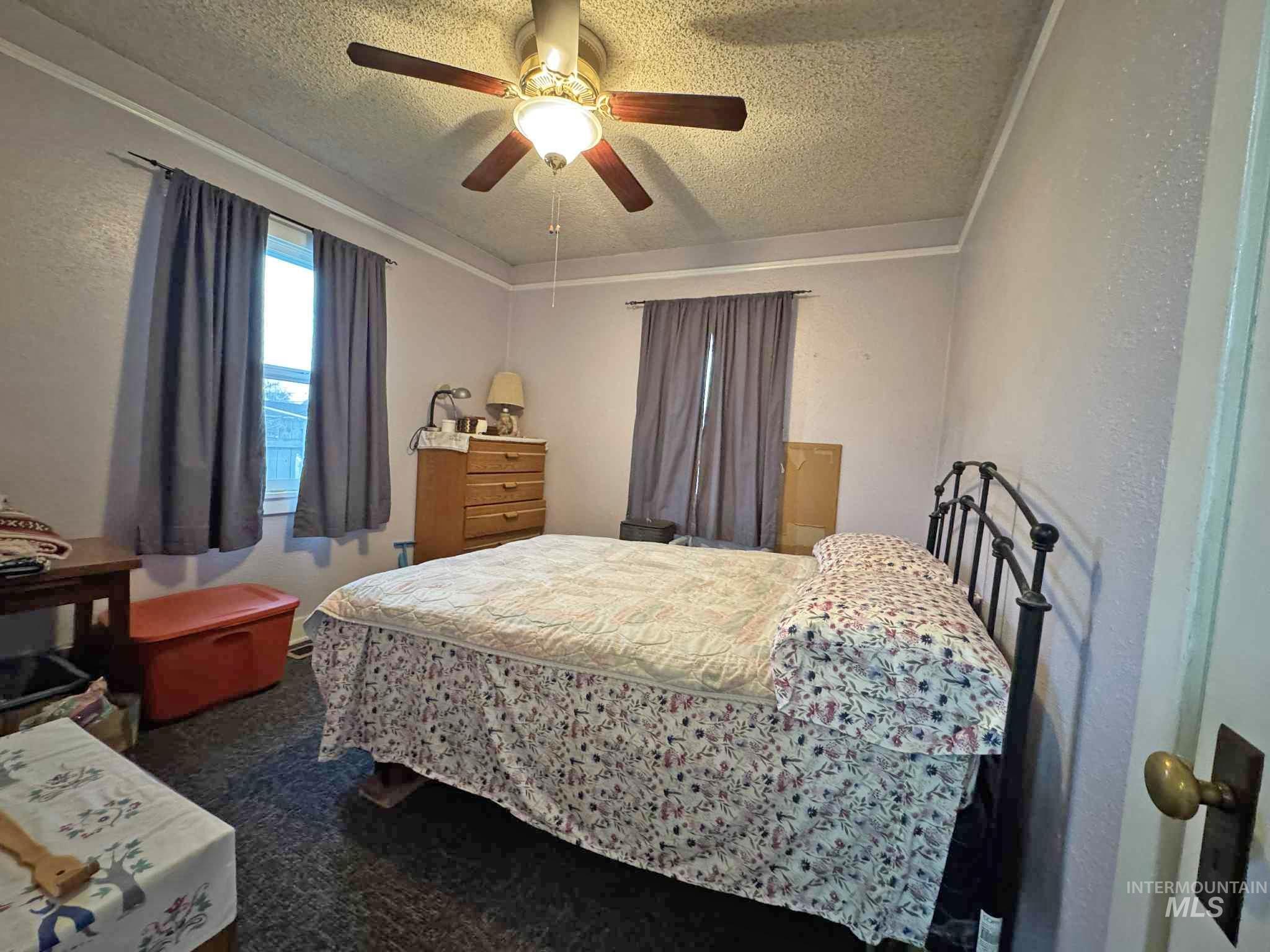 Bedroom featuring a textured ceiling, a ceiling fan, dark carpet, and a textured wall