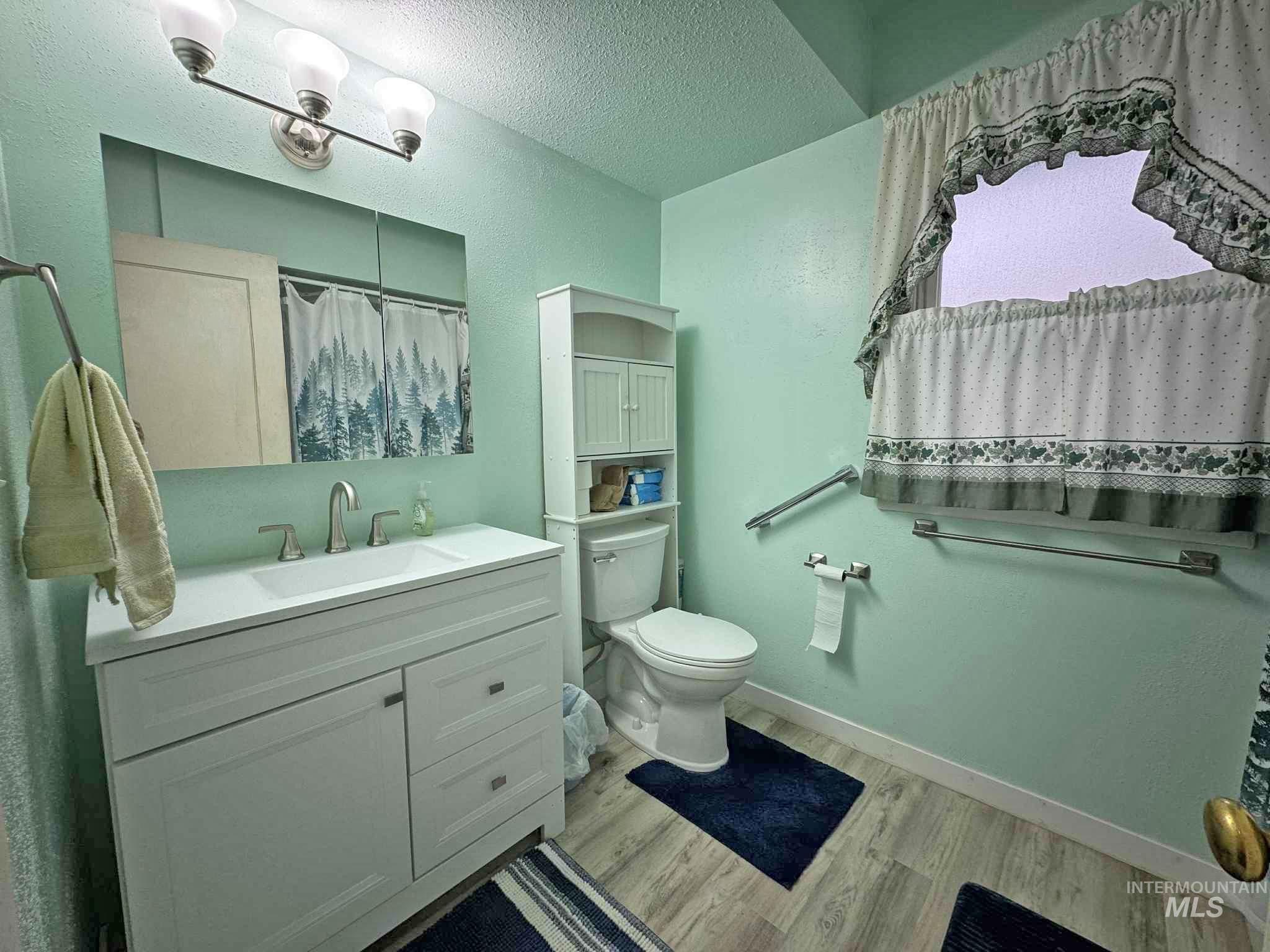 Bathroom featuring vanity, curtained shower, a textured ceiling, light wood-type flooring, and a textured wall