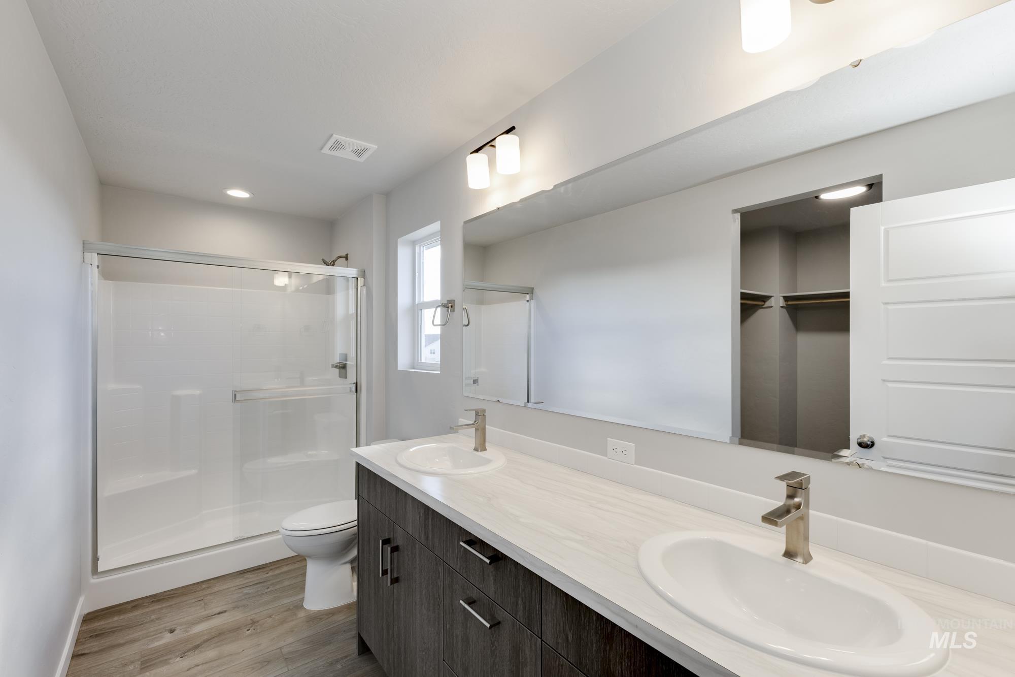 Bathroom featuring double vanity, light wood-style flooring, a shower stall, a spacious closet, and recessed lighting