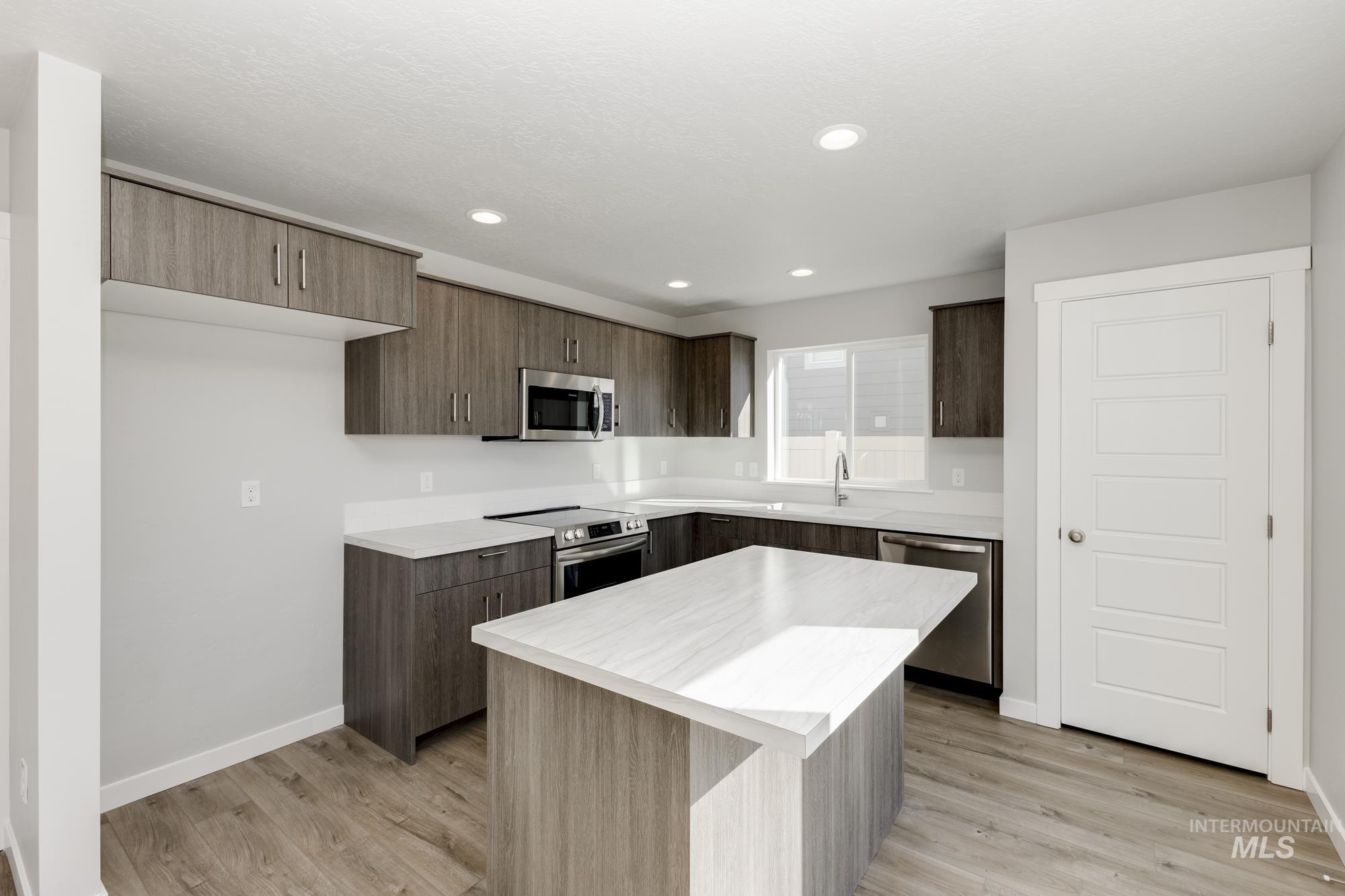Kitchen with light countertops, appliances with stainless steel finishes, modern cabinets, a kitchen island, and light wood finished floors