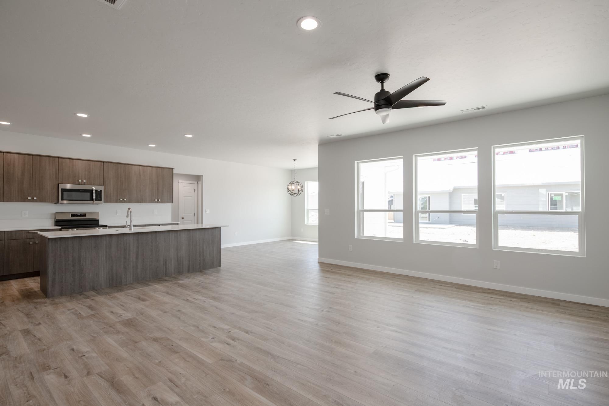 Kitchen featuring an island with sink, open floor plan, appliances with stainless steel finishes, light wood finished floors, and ceiling fan