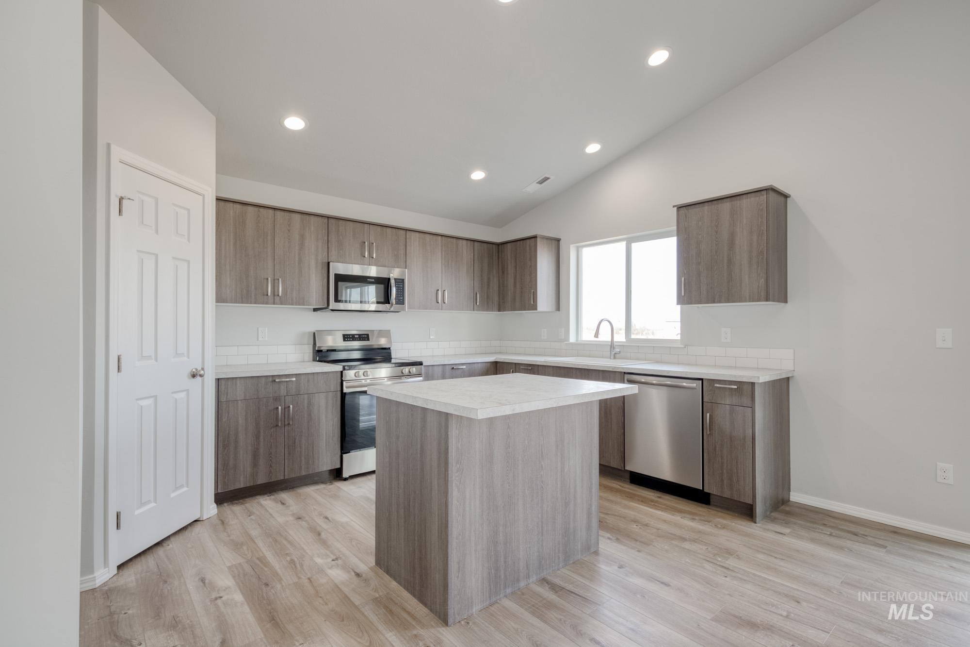 Kitchen featuring stainless steel appliances, light countertops, modern cabinets, a center island, and vaulted ceiling