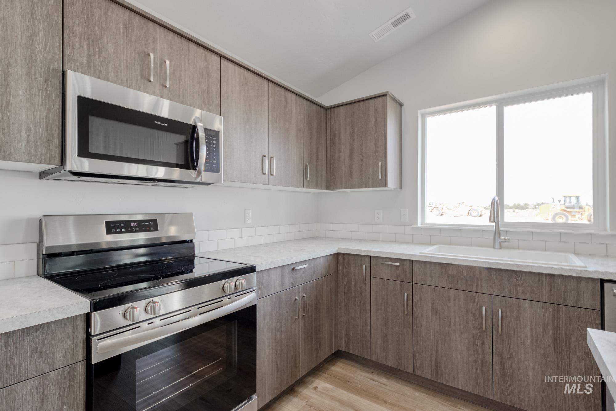 Kitchen with stainless steel appliances, light wood-style flooring, vaulted ceiling, and modern cabinets