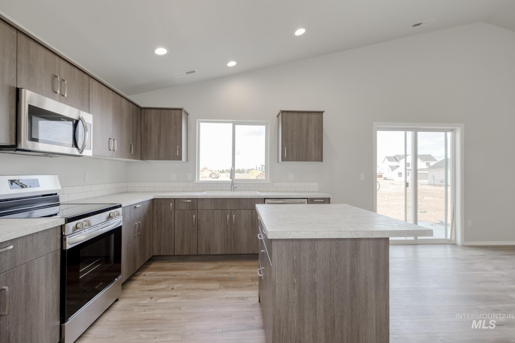 Kitchen featuring stainless steel appliances, vaulted ceiling, light countertops, light wood-type flooring, and a center island