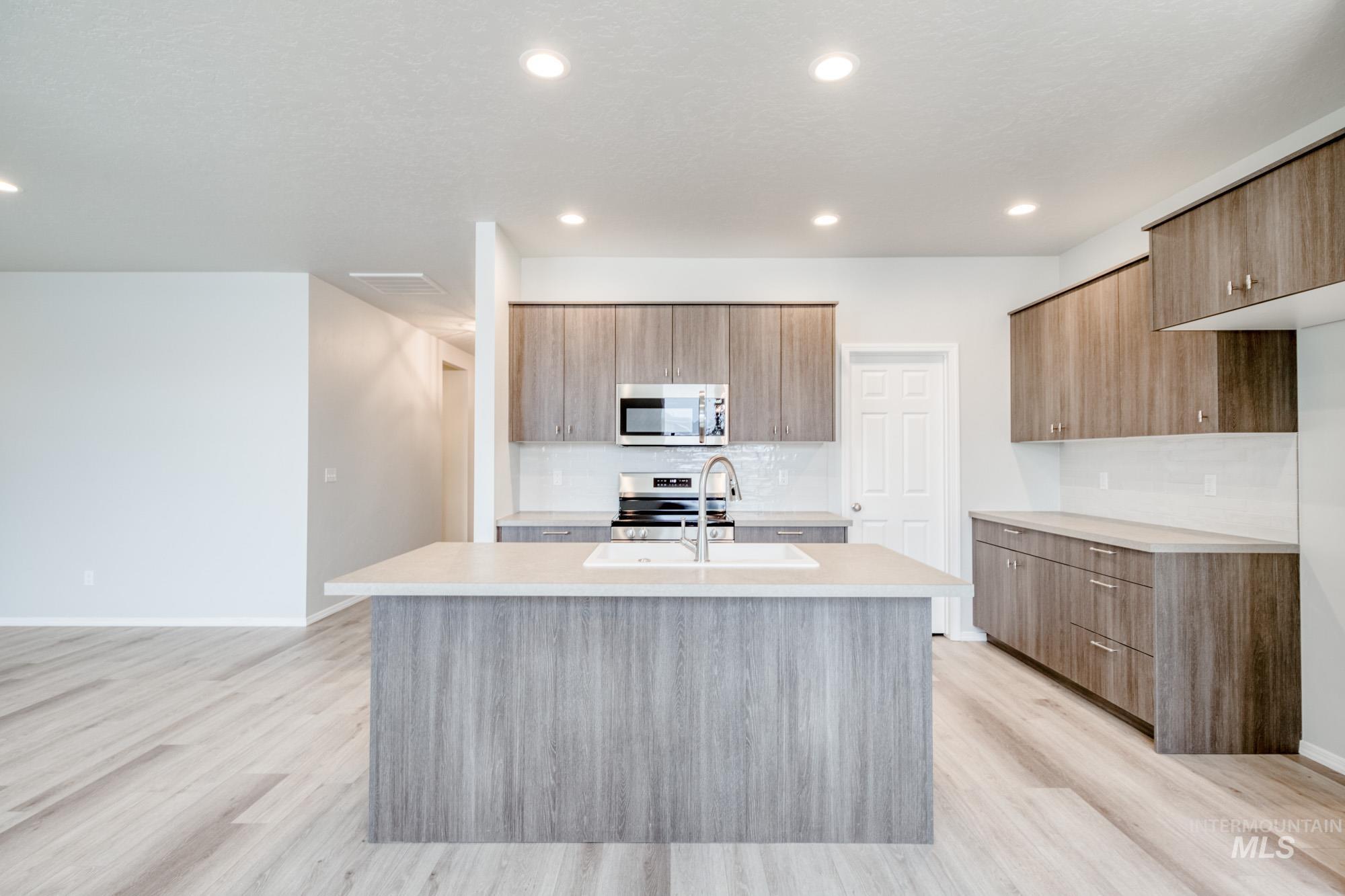 Kitchen with modern cabinets, stainless steel appliances, a kitchen island with sink, backsplash, and light wood-type flooring