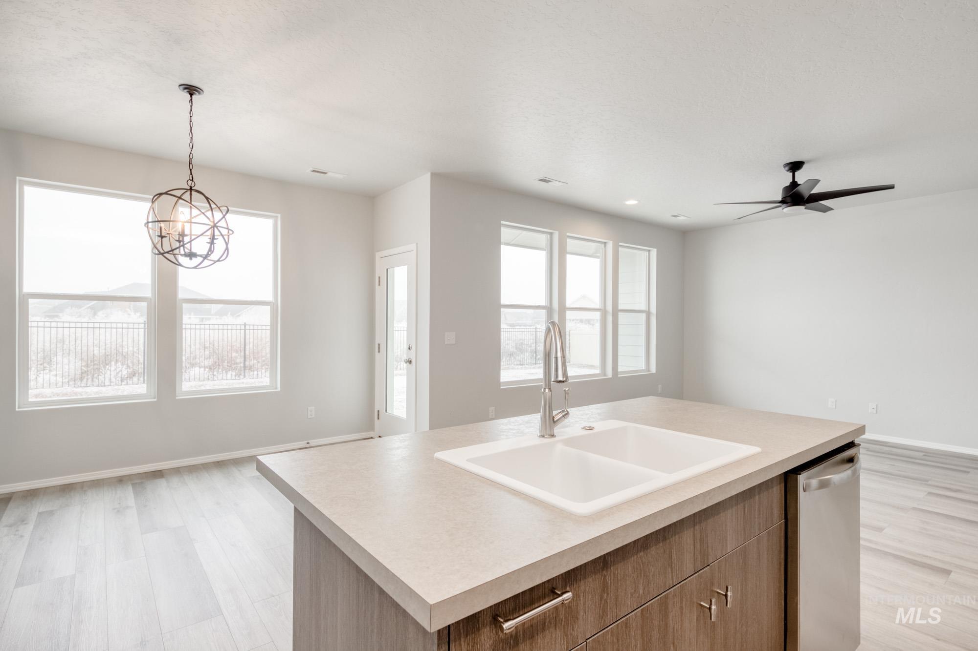 Kitchen featuring open floor plan, light wood-style floors, decorative light fixtures, light countertops, and an island with sink