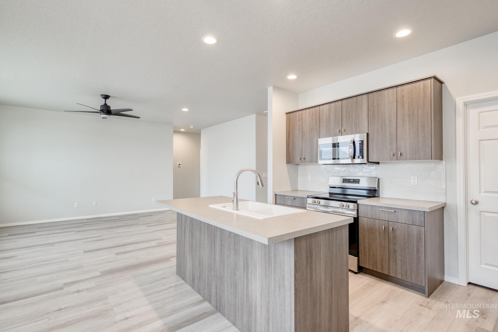 Kitchen with stainless steel appliances, a kitchen island with sink, light countertops, light wood-style flooring, and decorative backsplash