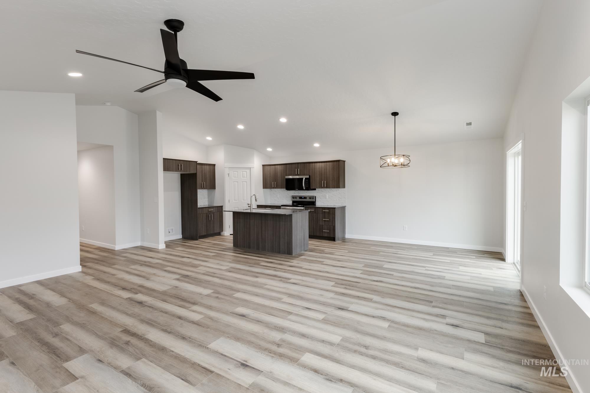 Unfurnished living room with light wood-style floors, ceiling fan, vaulted ceiling, a chandelier, and recessed lighting