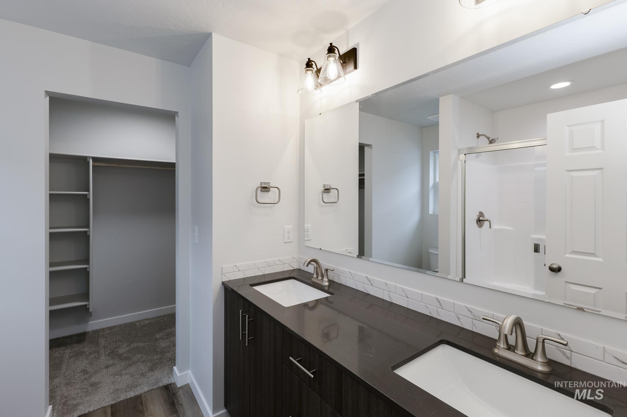 Bathroom featuring a walk in closet, a shower stall, double vanity, and dark wood-style floors
