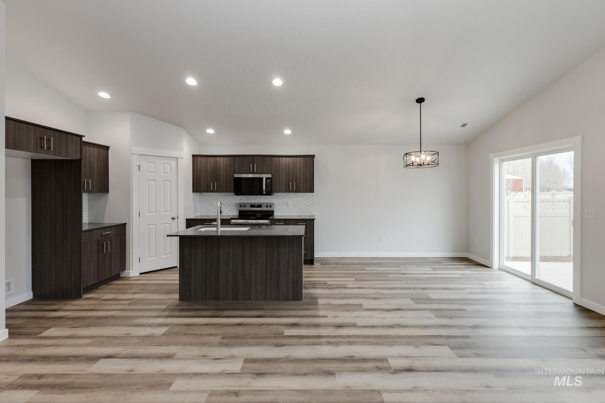 Kitchen featuring vaulted ceiling, dark brown cabinetry, stainless steel appliances, tasteful backsplash, and a center island with sink