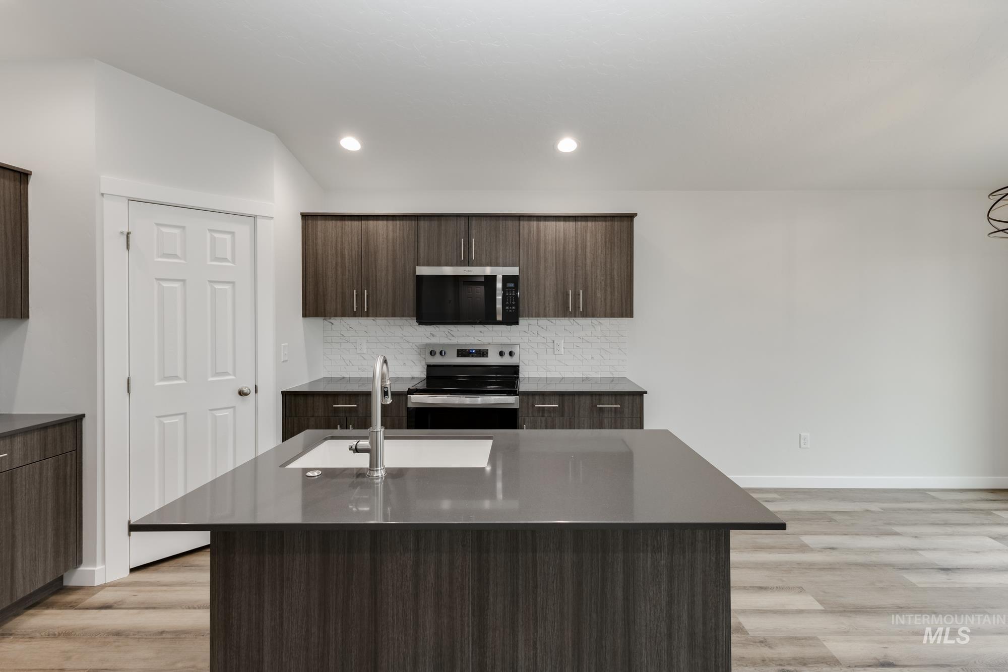 Kitchen featuring appliances with stainless steel finishes, dark brown cabinetry, a center island with sink, modern cabinets, and dark stone counters