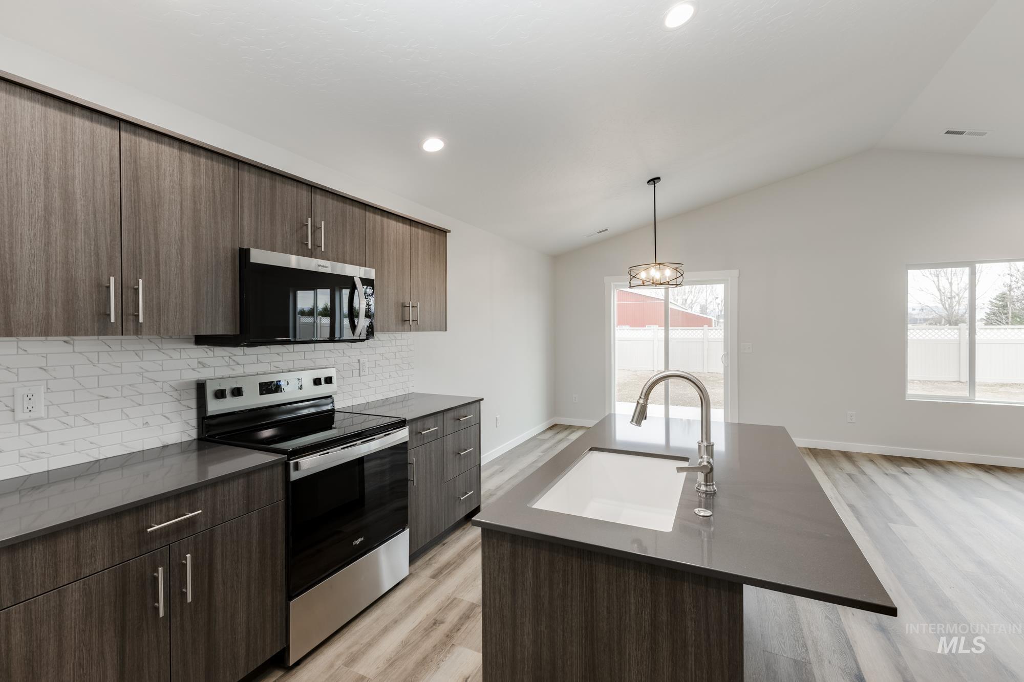 Kitchen with appliances with stainless steel finishes, pendant lighting, backsplash, modern cabinets, and a center island with sink