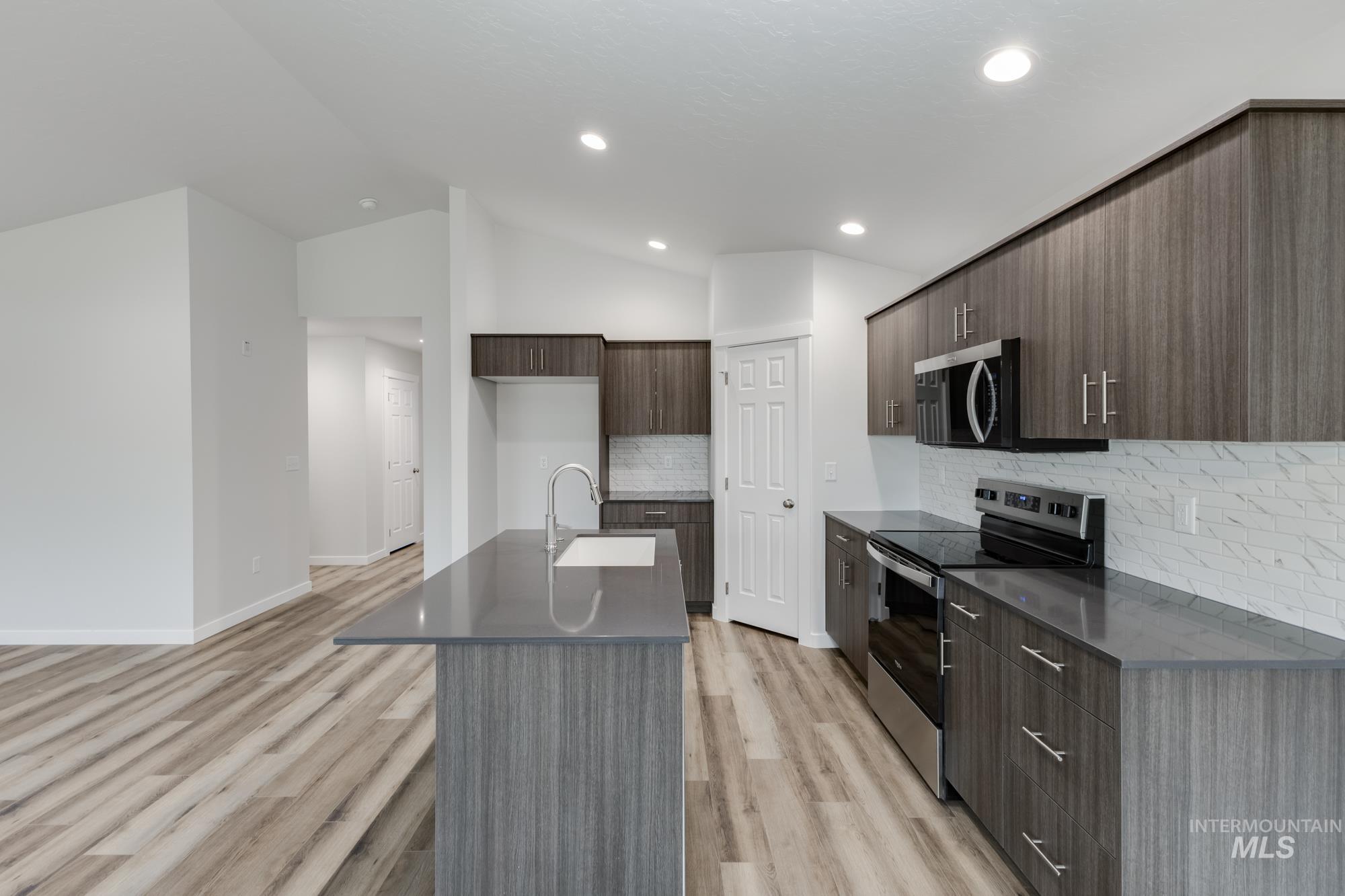 Kitchen with modern cabinets, stainless steel appliances, decorative backsplash, a kitchen island with sink, and light wood-style floors