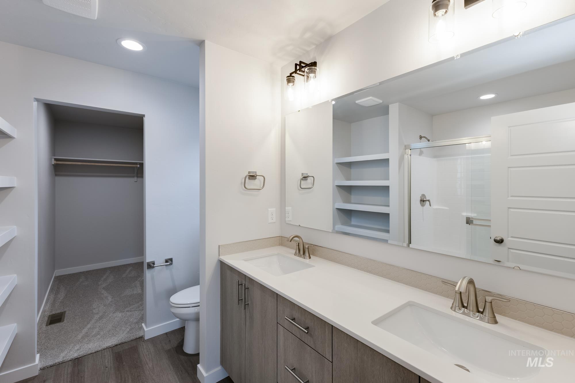 Bathroom featuring a walk in closet, double vanity, recessed lighting, a shower stall, and dark wood finished floors