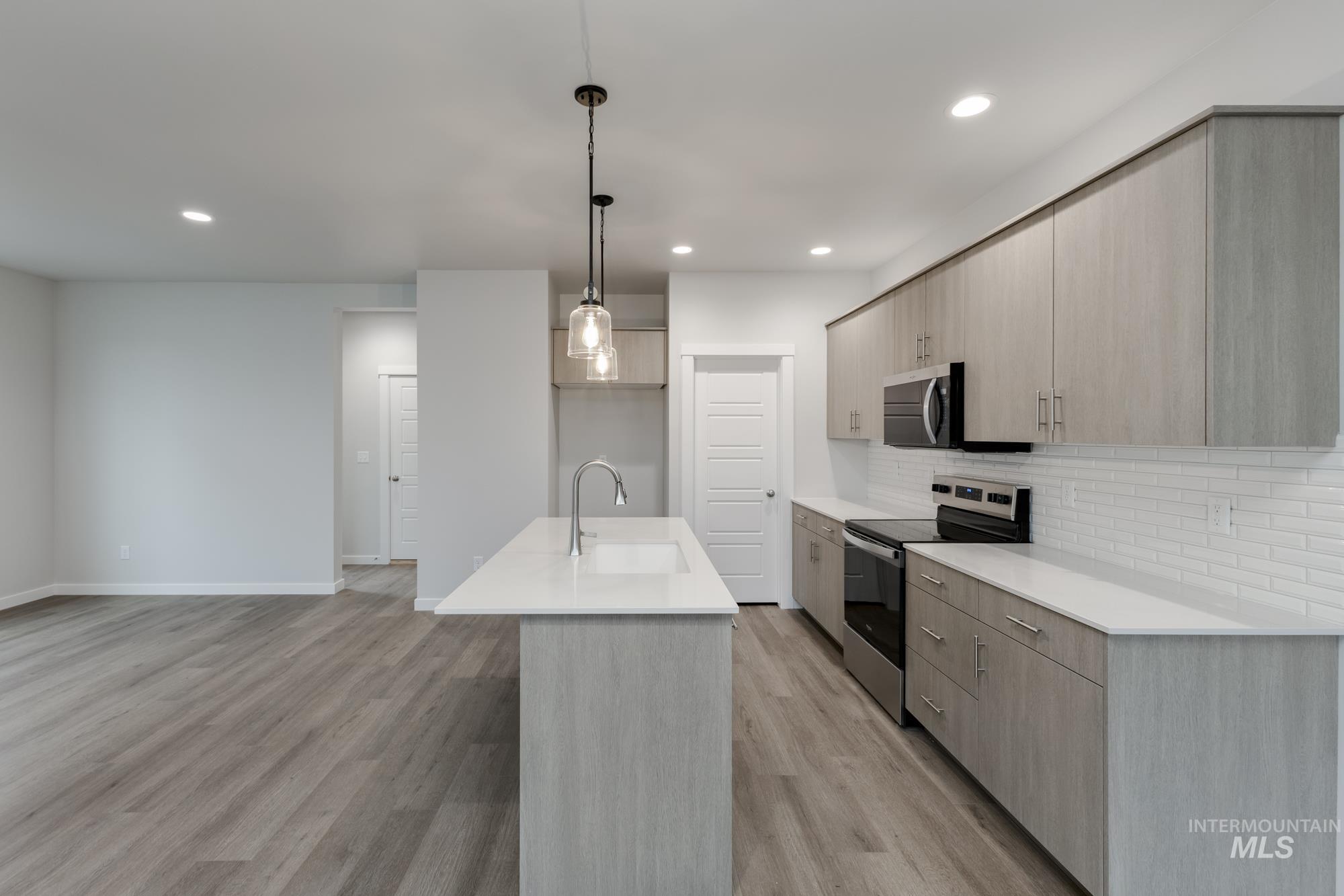 Kitchen featuring appliances with stainless steel finishes, modern cabinets, a center island with sink, decorative light fixtures, and light brown cabinetry