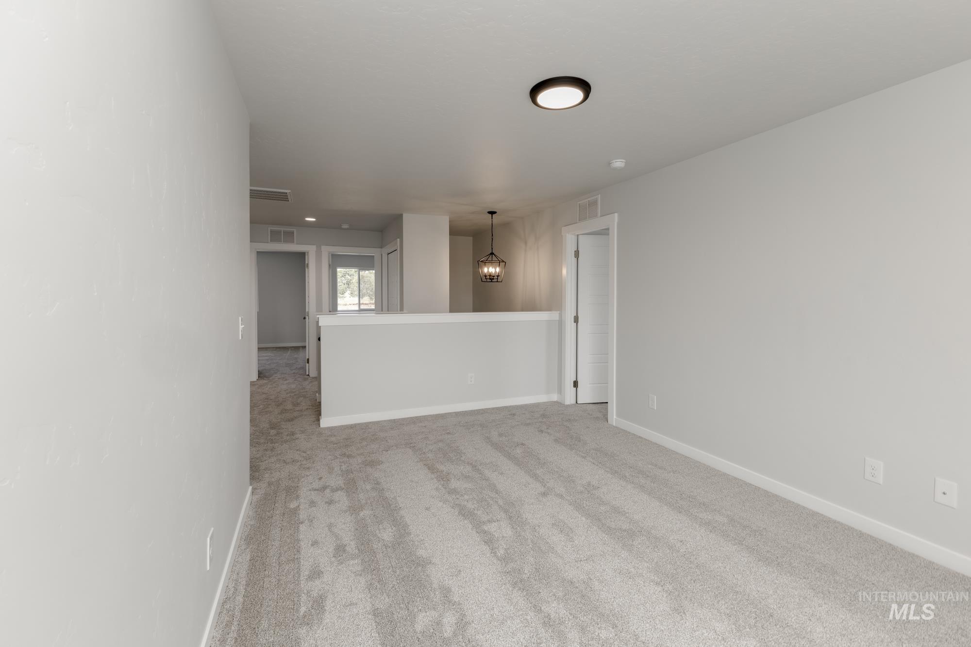 Unfurnished room featuring light colored carpet and a chandelier