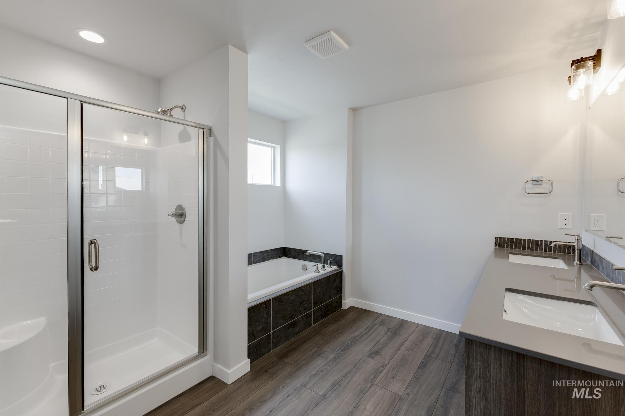Bathroom with dark wood finished floors, double vanity, a shower stall, and a garden tub