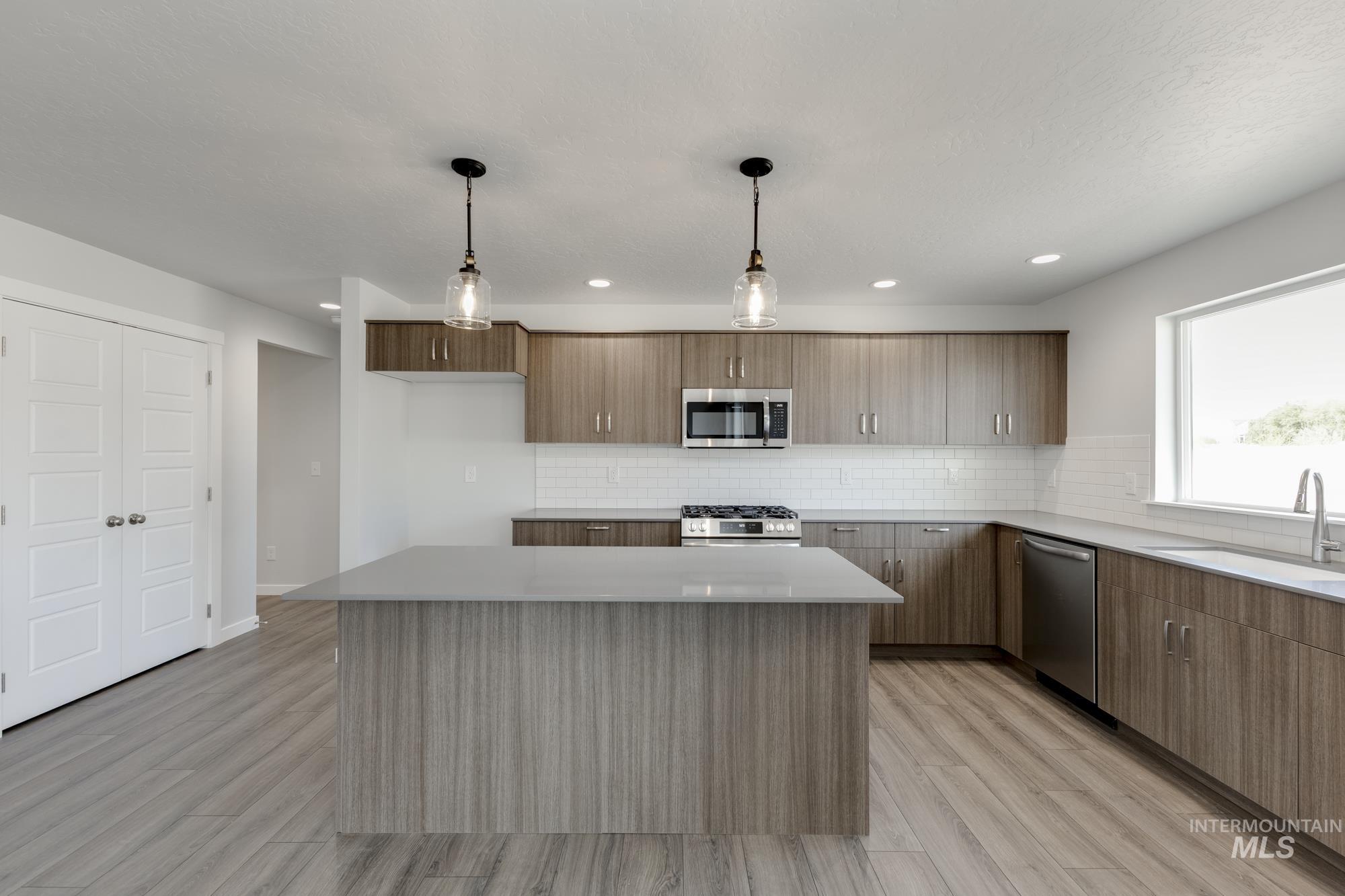 Kitchen featuring tasteful backsplash, hanging light fixtures, a center island, light wood-style flooring, and appliances with stainless steel finishes