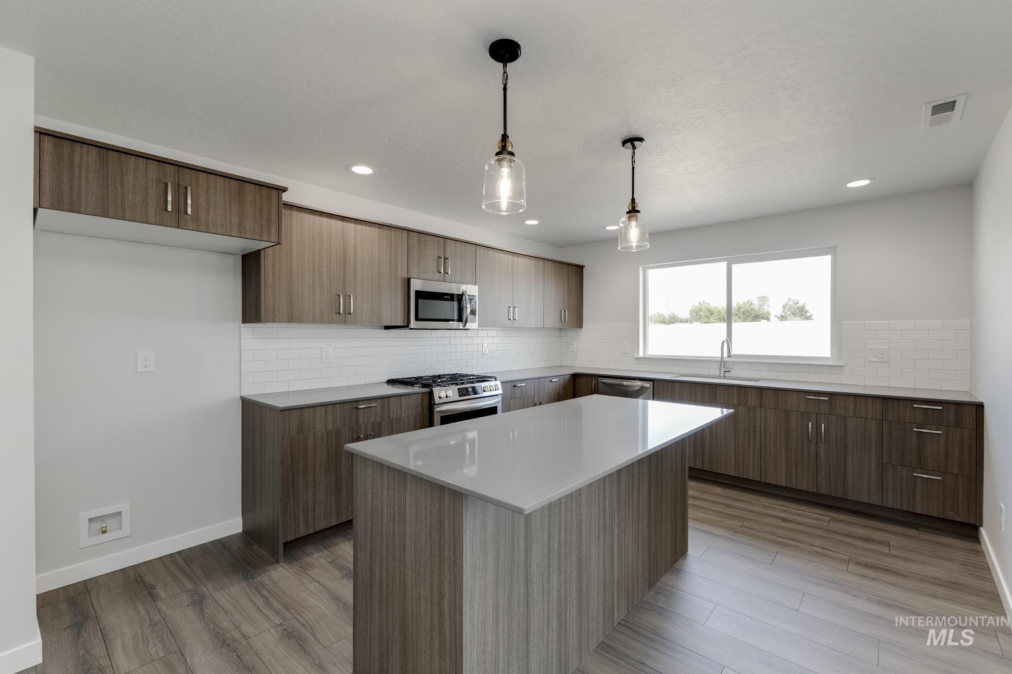 Kitchen featuring backsplash, decorative light fixtures, appliances with stainless steel finishes, light wood-style floors, and recessed lighting