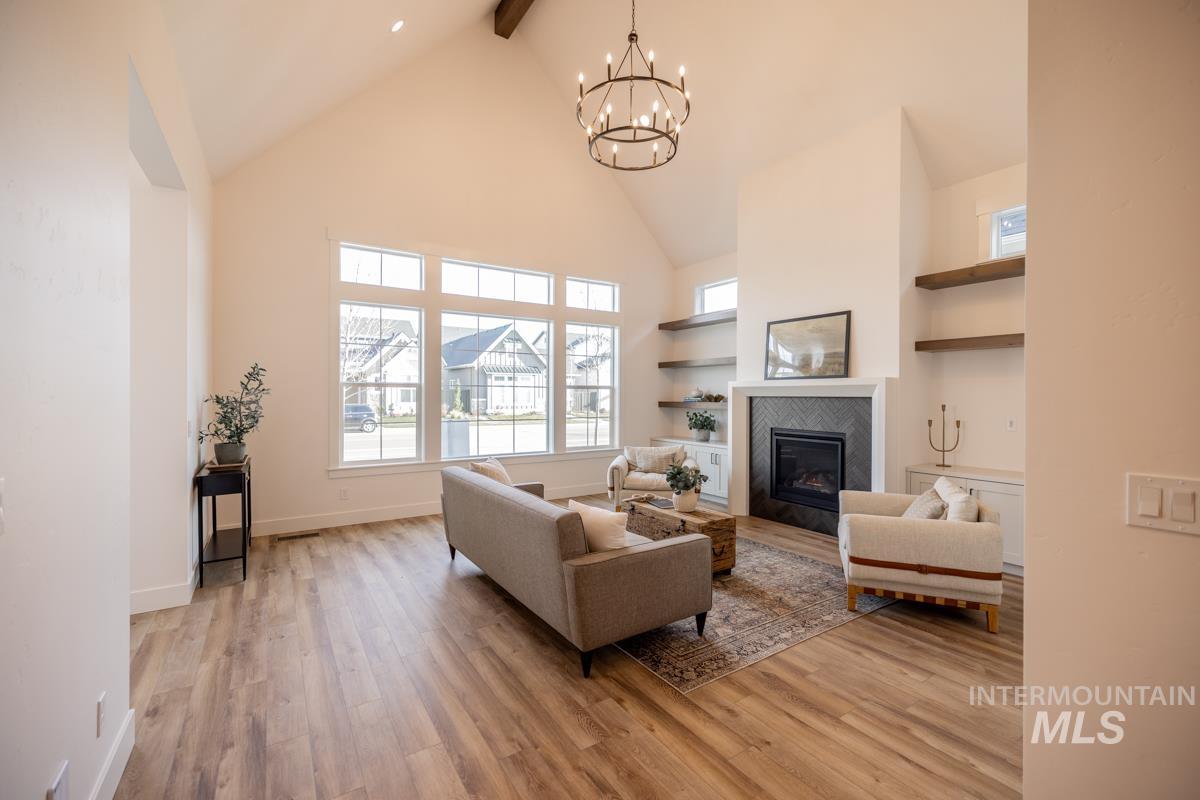 Living area with built in shelves, high vaulted ceiling, light wood-type flooring, beam ceiling, and a tiled fireplace