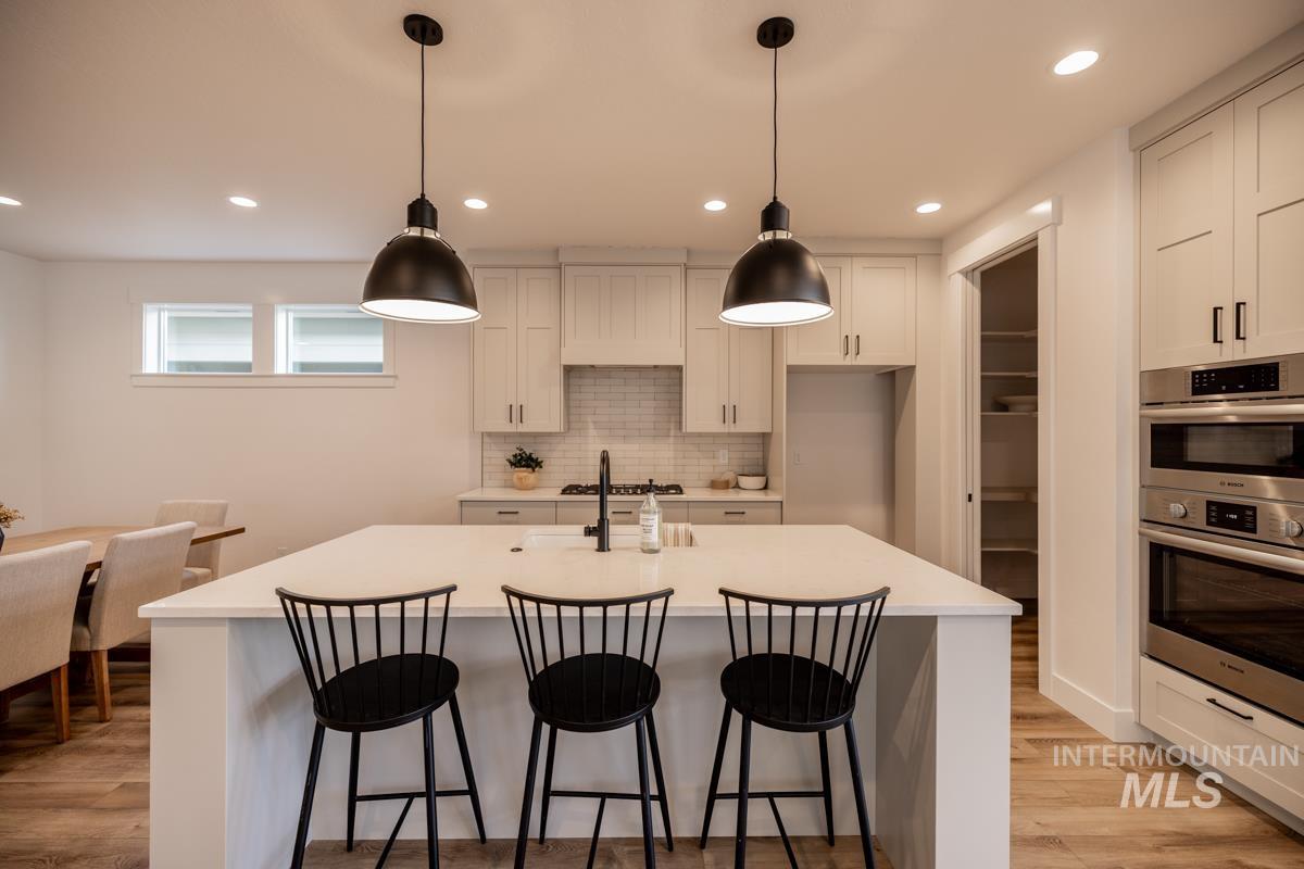 Kitchen with recessed lighting, decorative light fixtures, a breakfast bar, backsplash, and light wood-style floors