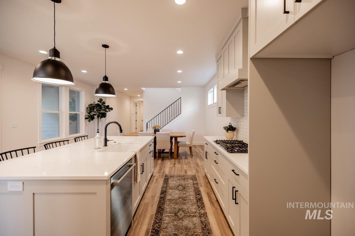 Kitchen featuring white cabinets, backsplash, pendant lighting, light wood finished floors, and appliances with stainless steel finishes