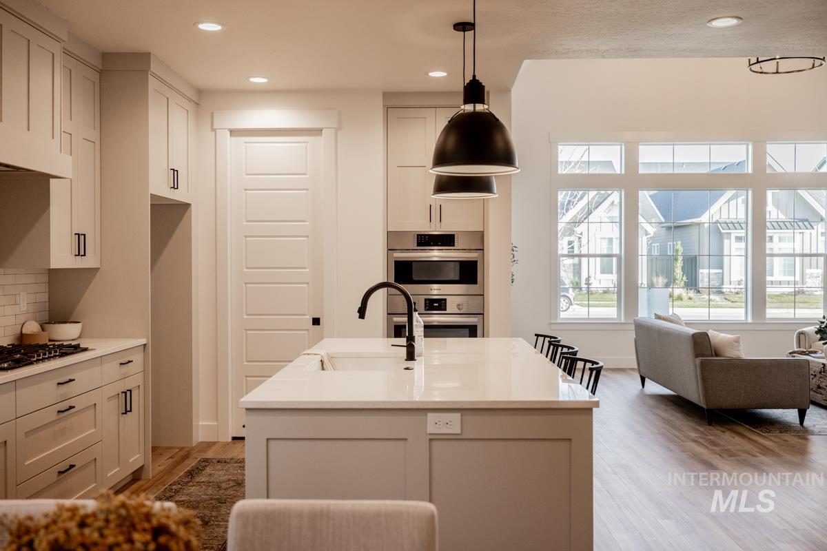 Kitchen featuring an island with sink, light stone countertops, recessed lighting, stainless steel appliances, and hanging light fixtures