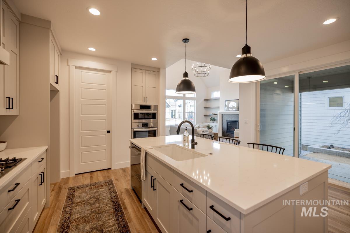 Kitchen featuring white cabinets, a kitchen island with sink, light wood-type flooring, light stone countertops, and recessed lighting
