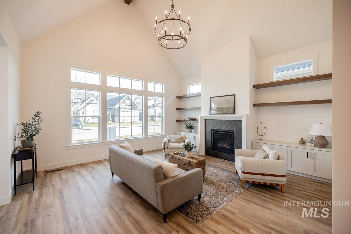 Living room with high vaulted ceiling, a fireplace, light wood-type flooring, a chandelier, and beamed ceiling
