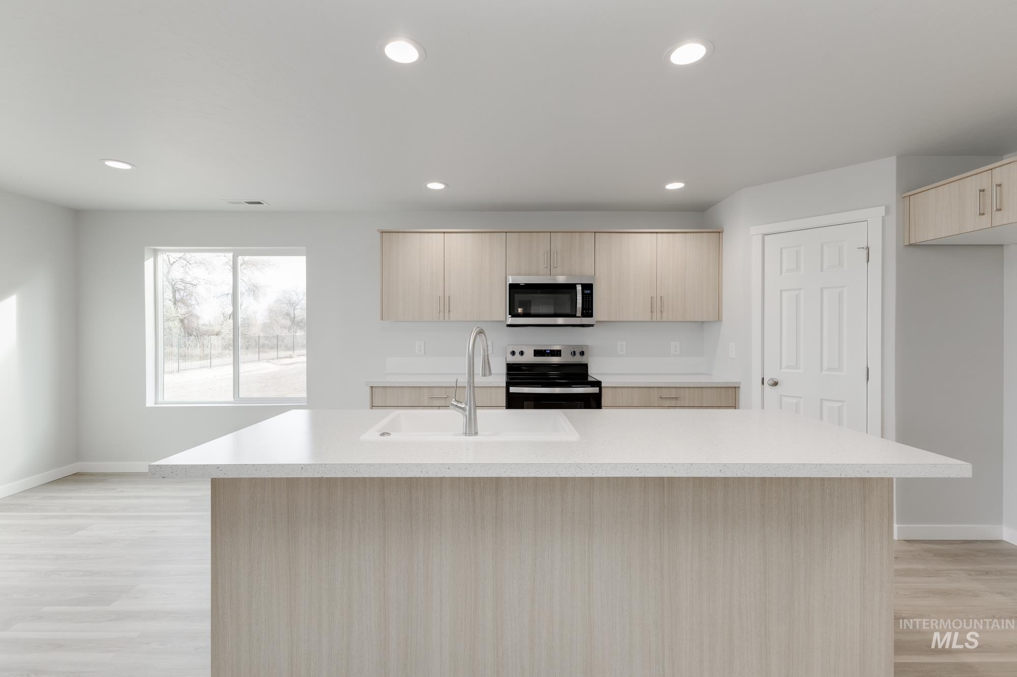 Kitchen with light brown cabinets, an island with sink, stainless steel appliances, light wood-style floors, and recessed lighting