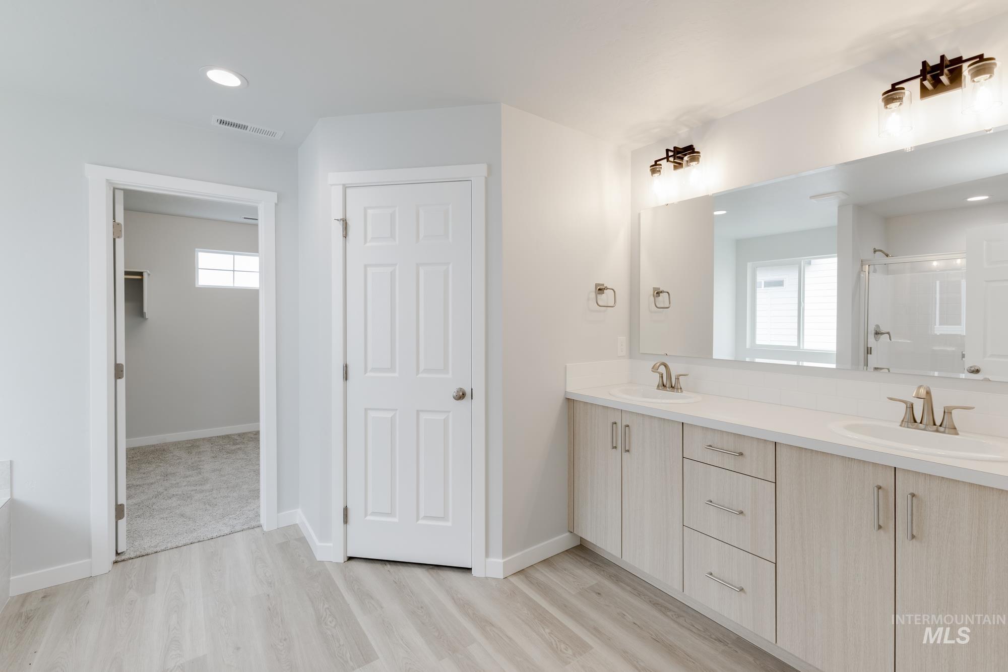 Bathroom featuring double vanity, a shower stall, a walk in closet, recessed lighting, and light wood-style floors